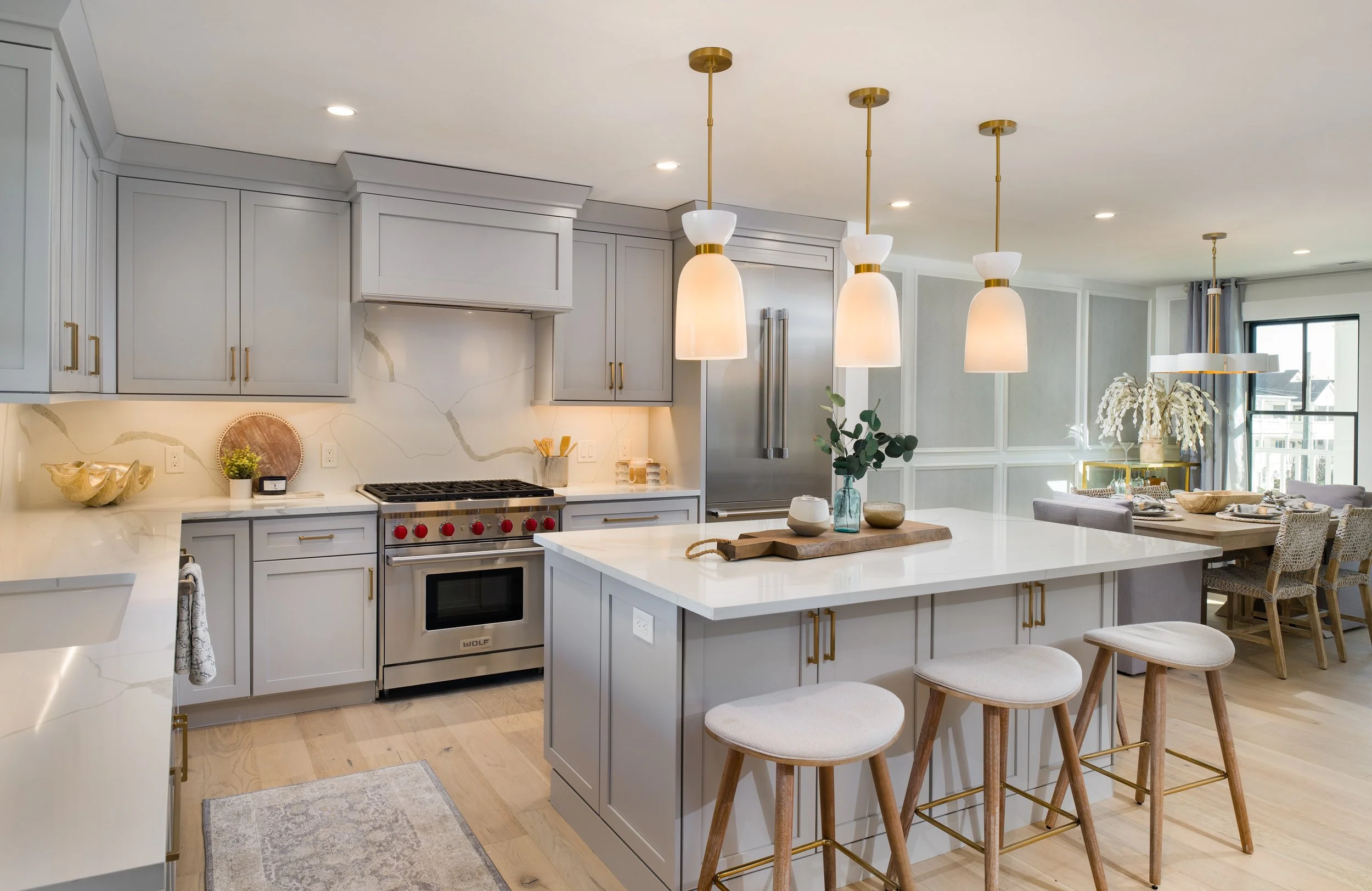 Modern kitchen with white cabinets, an island with barstools, pendant lights, and a dining area in the background.