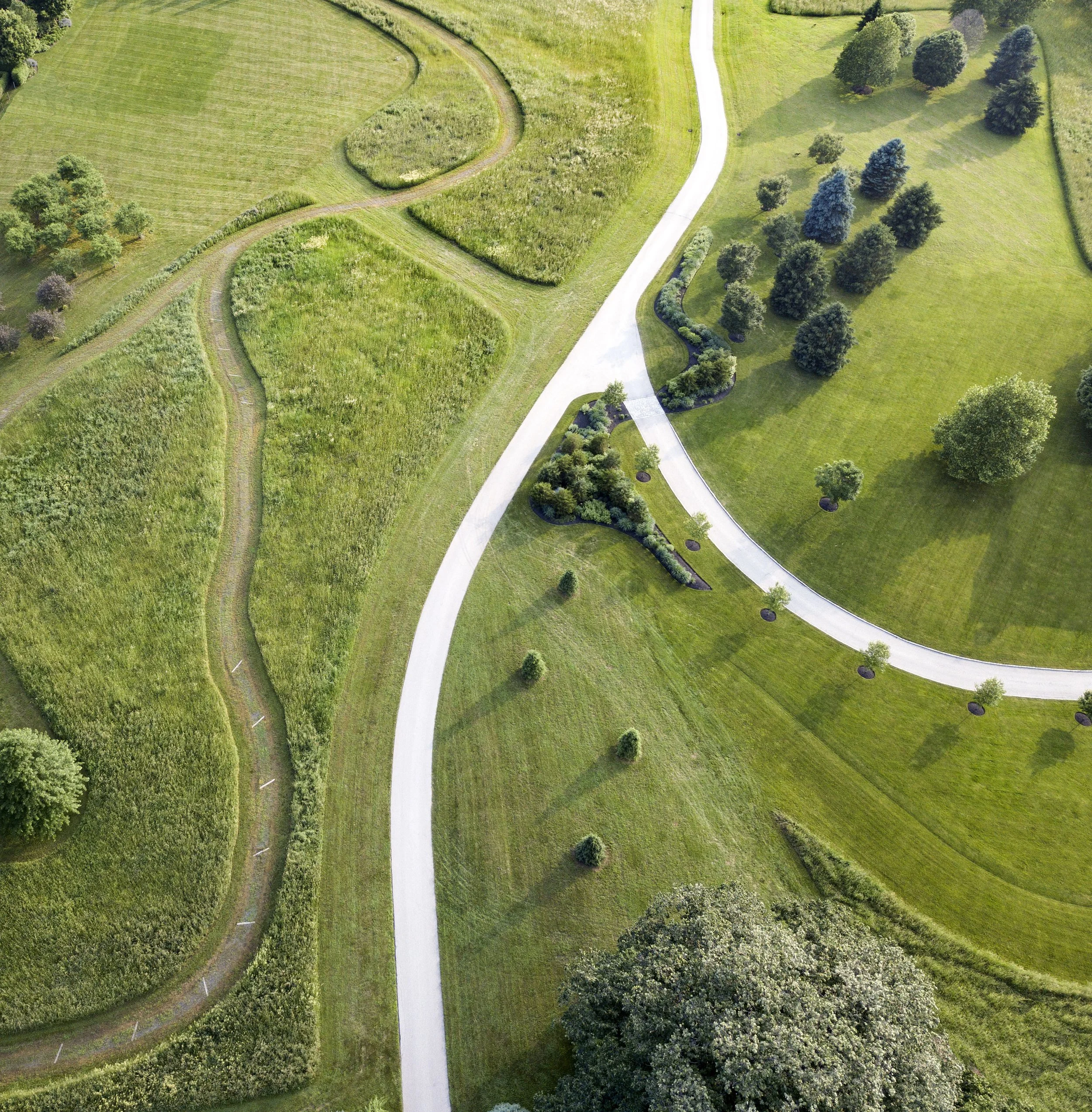 Aerial view of a landscaped rural property with winding paved driveways, mowed lawns, trees, gardens, and surrounding fields