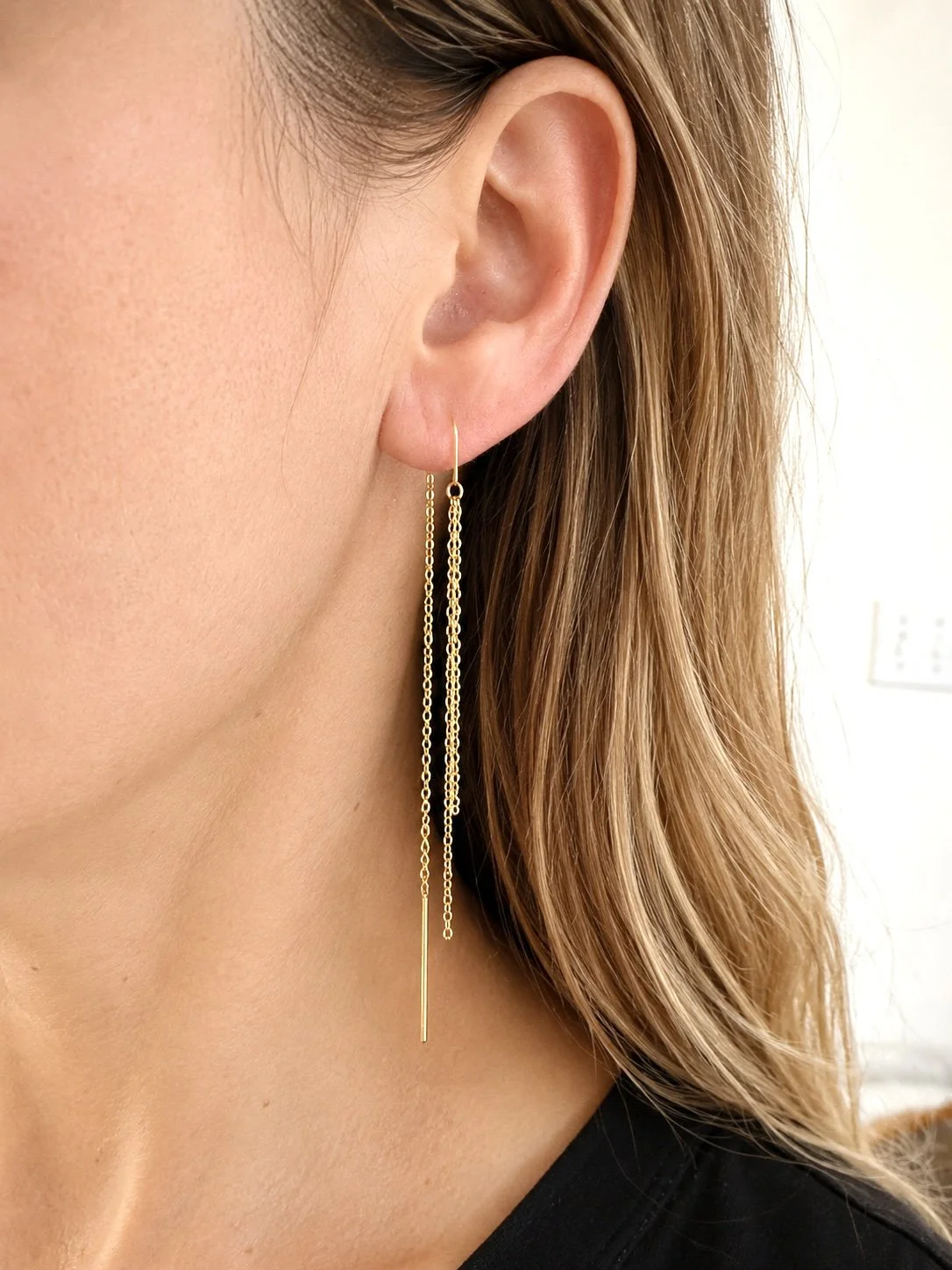 Femme portant les boucles d’oreilles pendantes Filia en acier inoxydable doré avec fines chaînes délicates. - Tokade