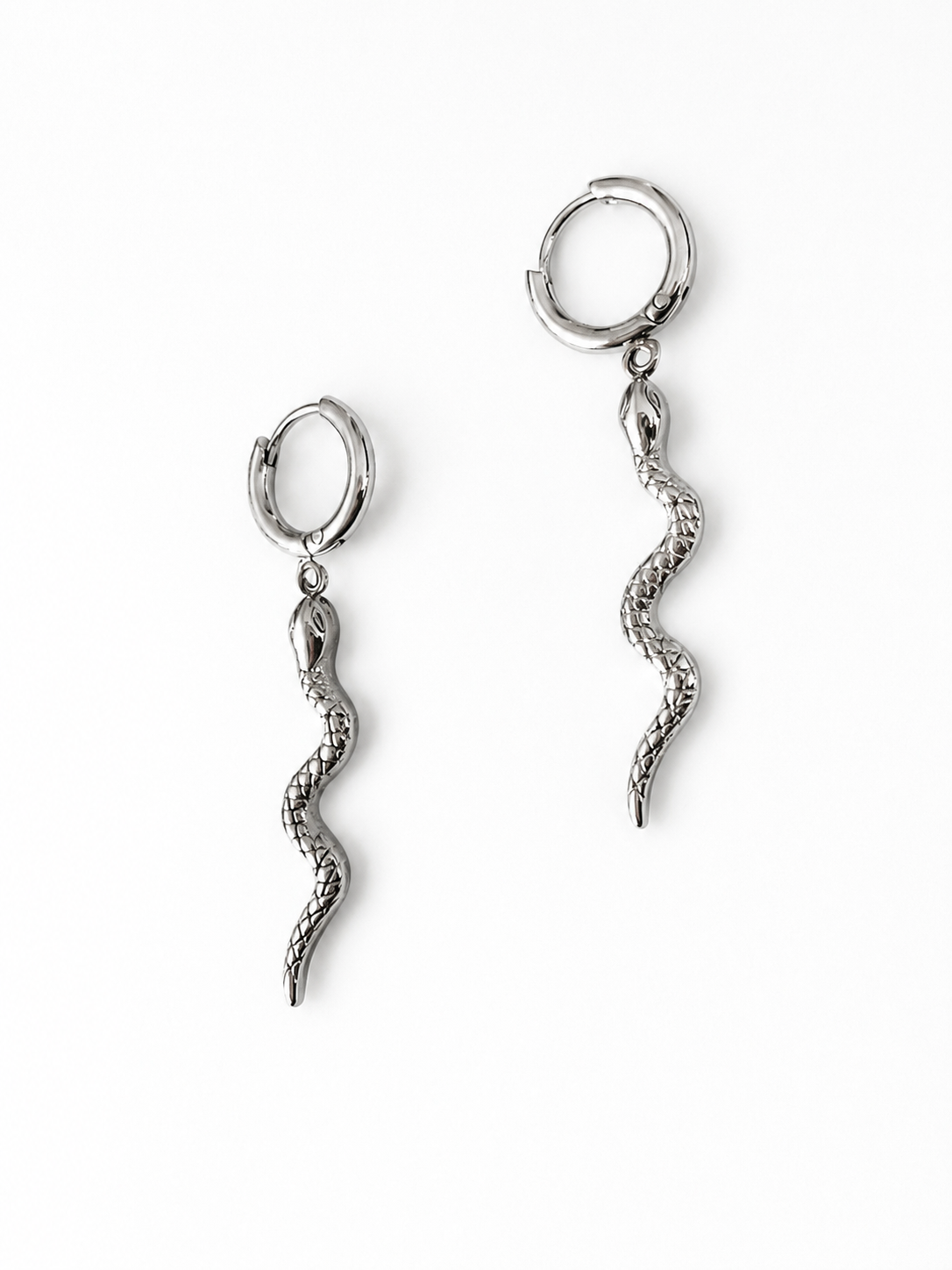Boucles d’oreilles Médusa en acier inoxydable argenté composées d’anneaux avec pendentifs en forme de serpent sur fond blanc.
