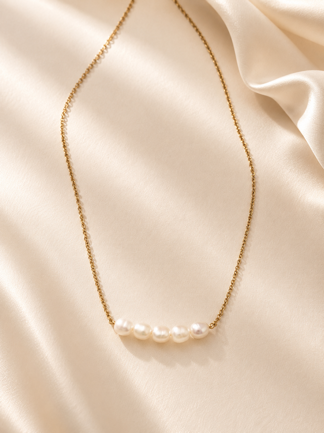 Collier Cristy en acier inoxydable doré et perles d’eau douce présenté sur un tissu satiné crème. - Tokade