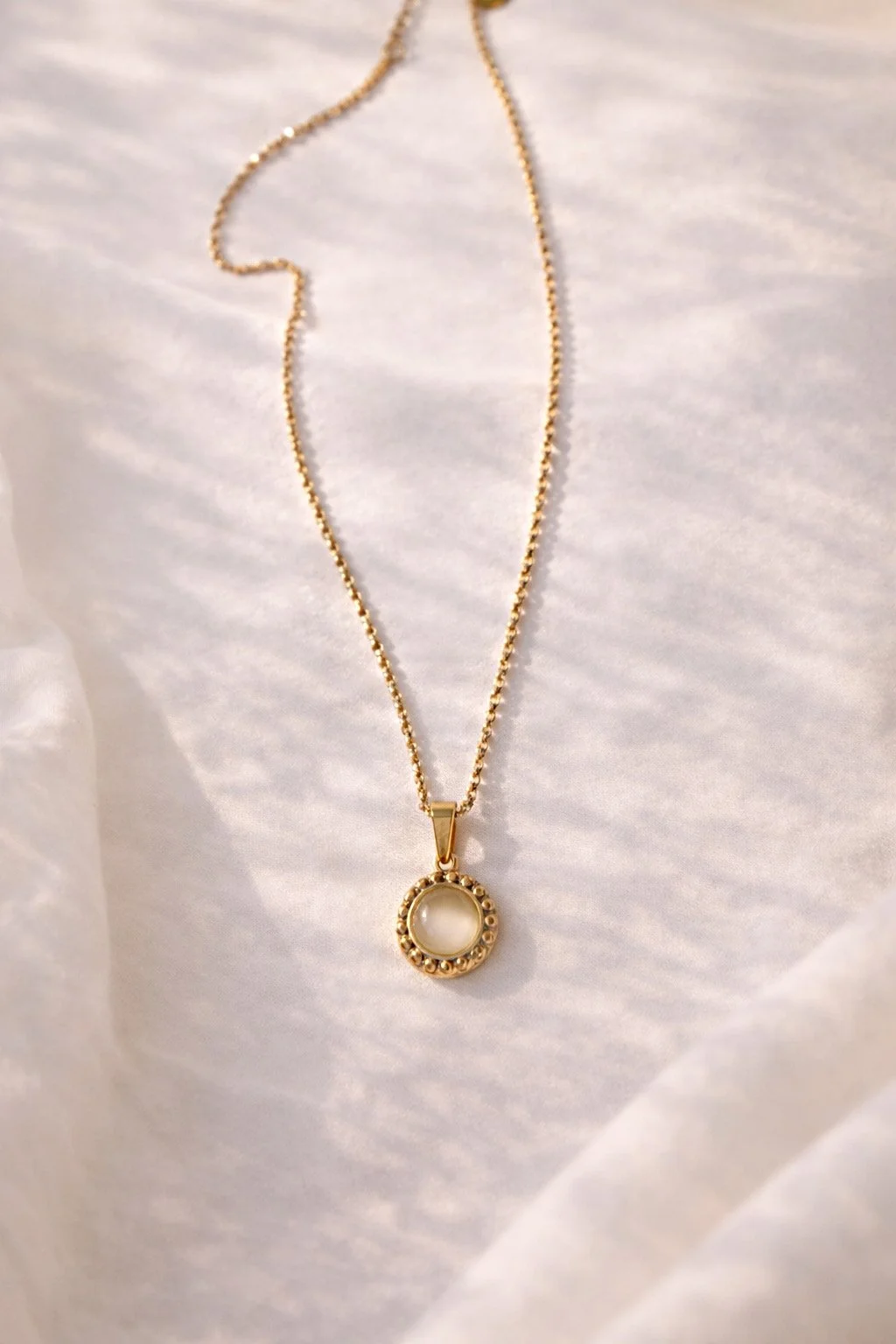 Collier doré avec pierre nacrée présenté sur tissu lumineux-Tokade