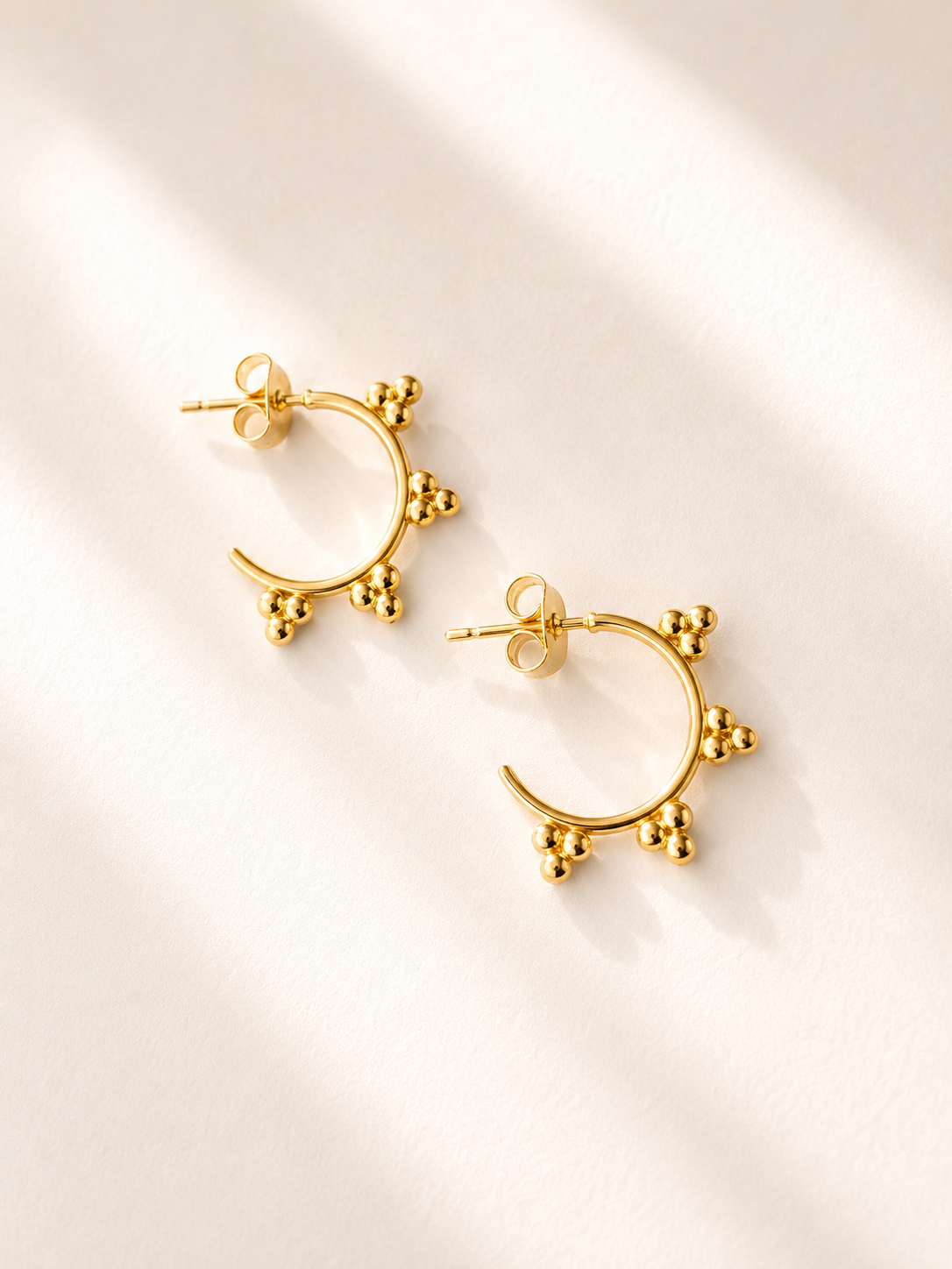 Paire de boucles d’oreilles Juli en acier inoxydable doré avec anneaux décorés de petites billes sur fond blanc.