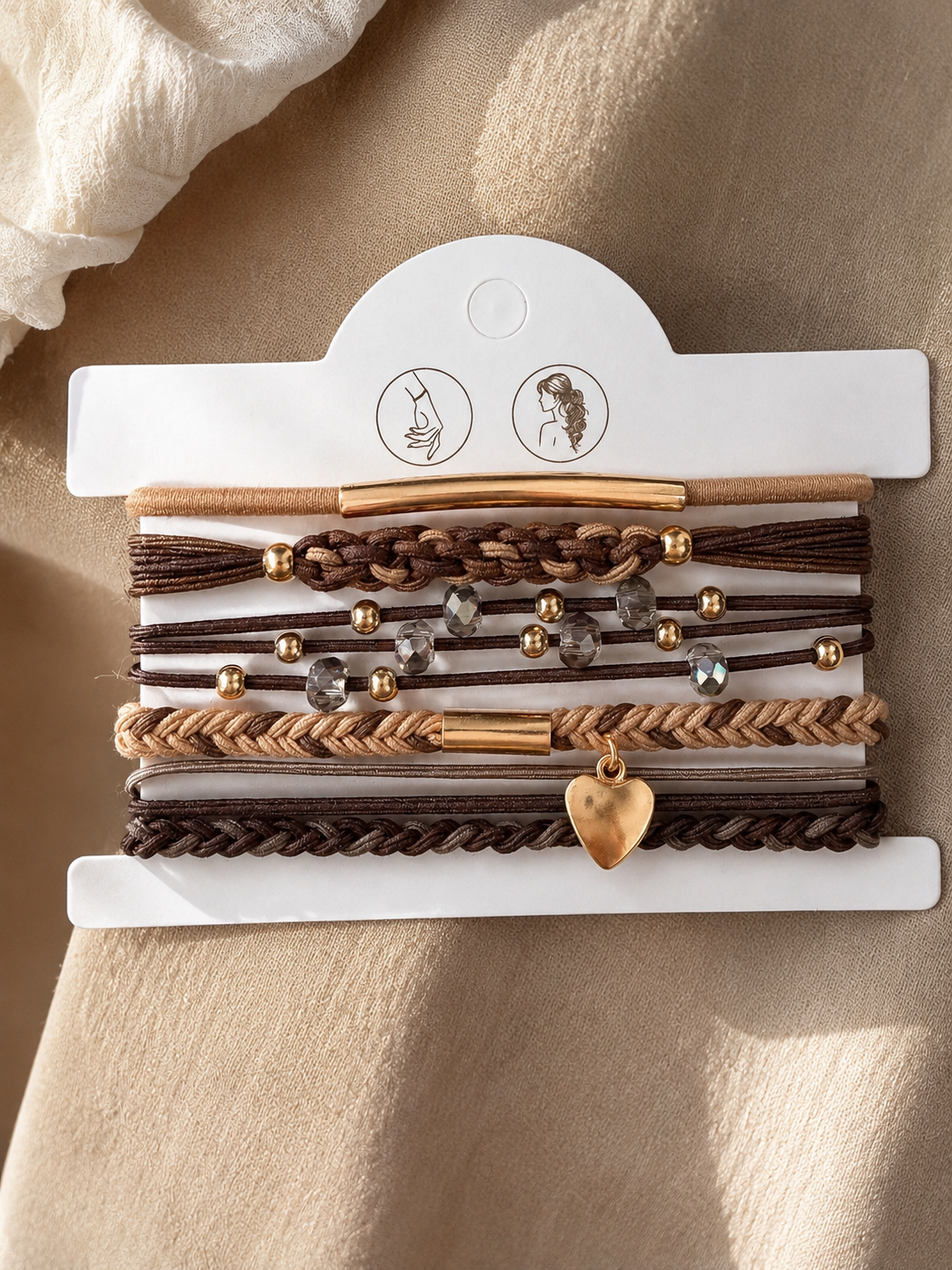 Lot de 5 élastiques à cheveux et bracelets 2-en-1 bohèmes en brun, beige et doré avec cristaux, tresses, perles et pendentif cœur, portés au poignet.