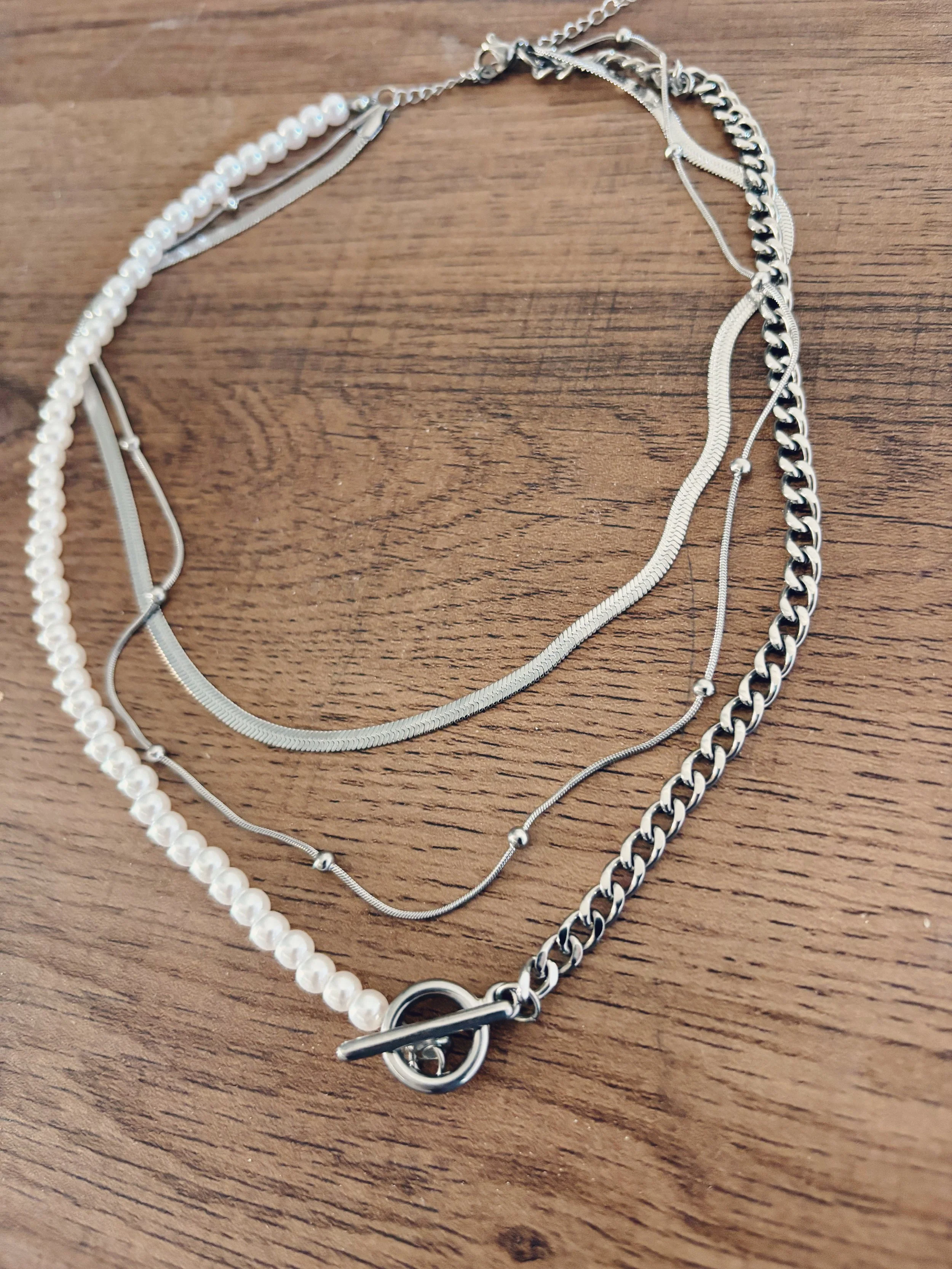 Gros plan du collier posé sur une surface en bois, détaillant la texture et la finition des différentes chaînes.