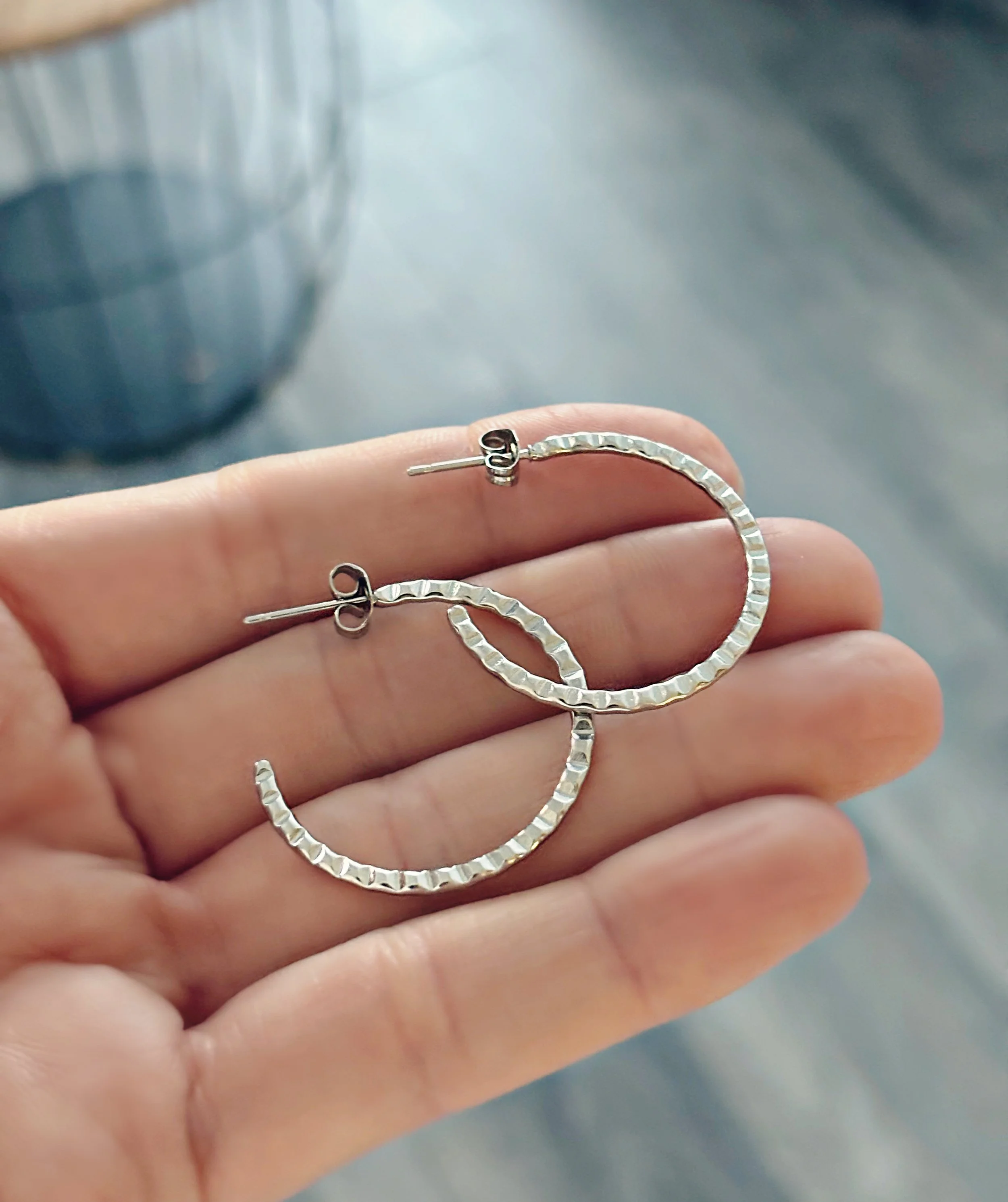 Boucles d’oreilles Aïna en acier inoxydable texturé, anneaux argentés scintillants posés dans une main – Tokade