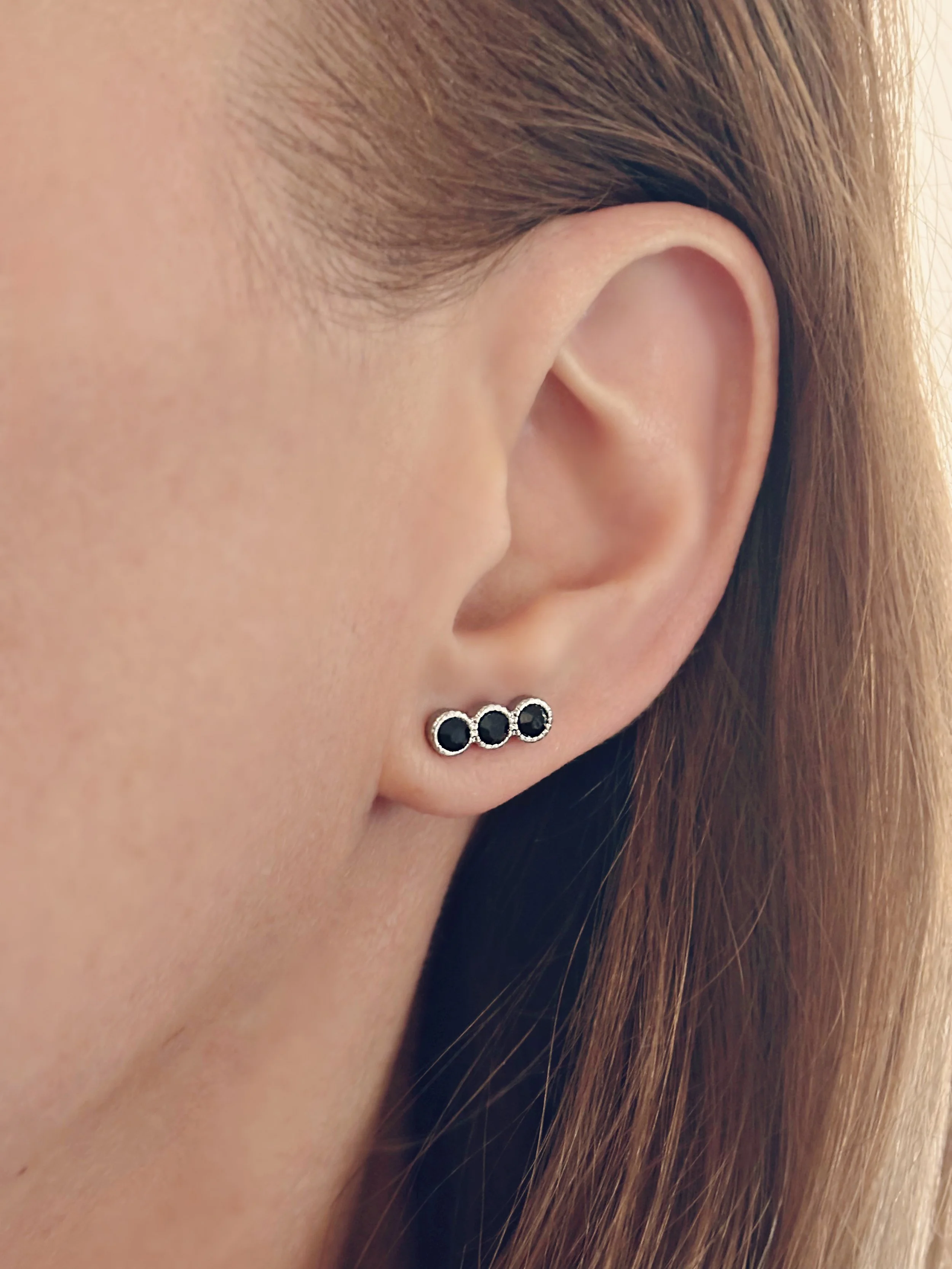 Boucles Liora portées, mettant en valeur les trois pierres noires discrètes et brillantes.
