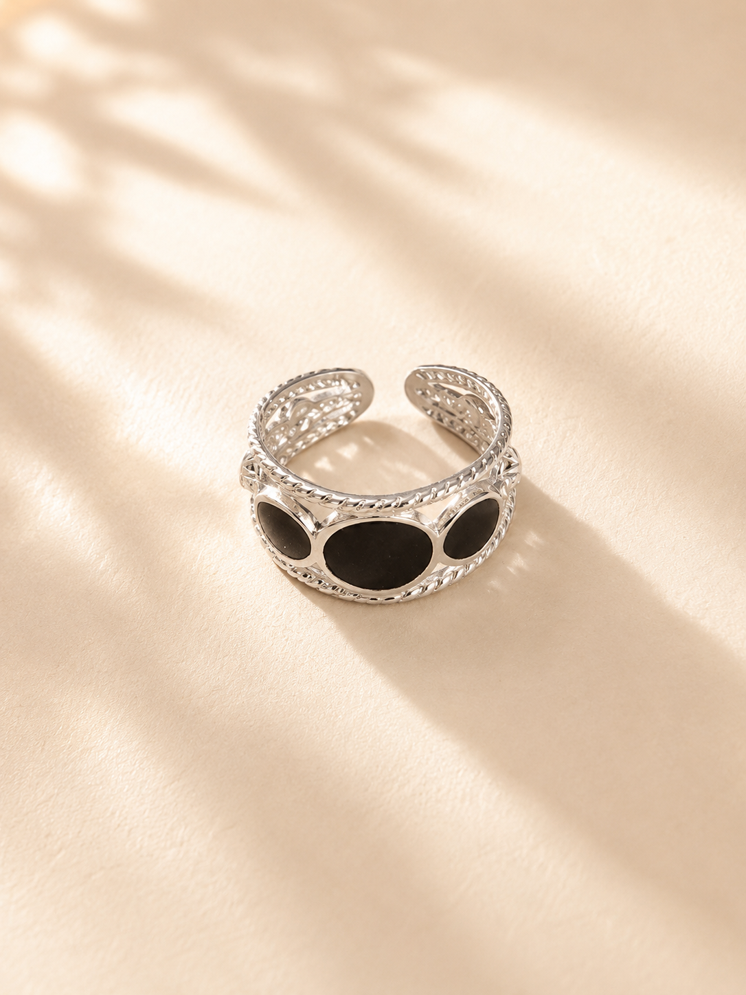 Bague Femina en acier inoxydable argenté avec pierres noires présentée sur un tissu crème lumineux. - Tokade