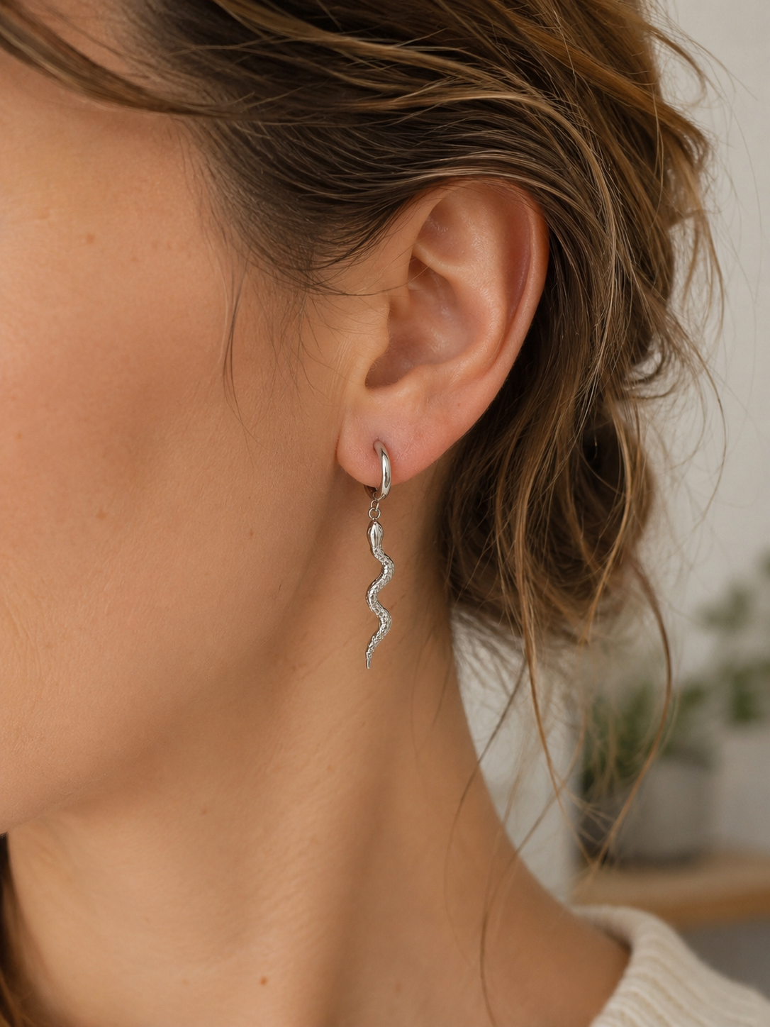 Femme portant les boucles d’oreilles Médusa en acier inoxydable argenté avec pendentif serpent.