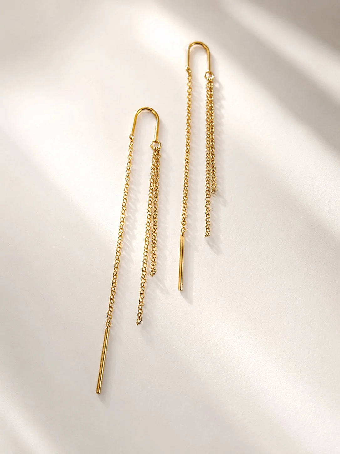 Boucles d’oreilles Filia en acier inoxydable doré avec tige traversante et fines chaînes pendantes sur fond blanc. - Tokade