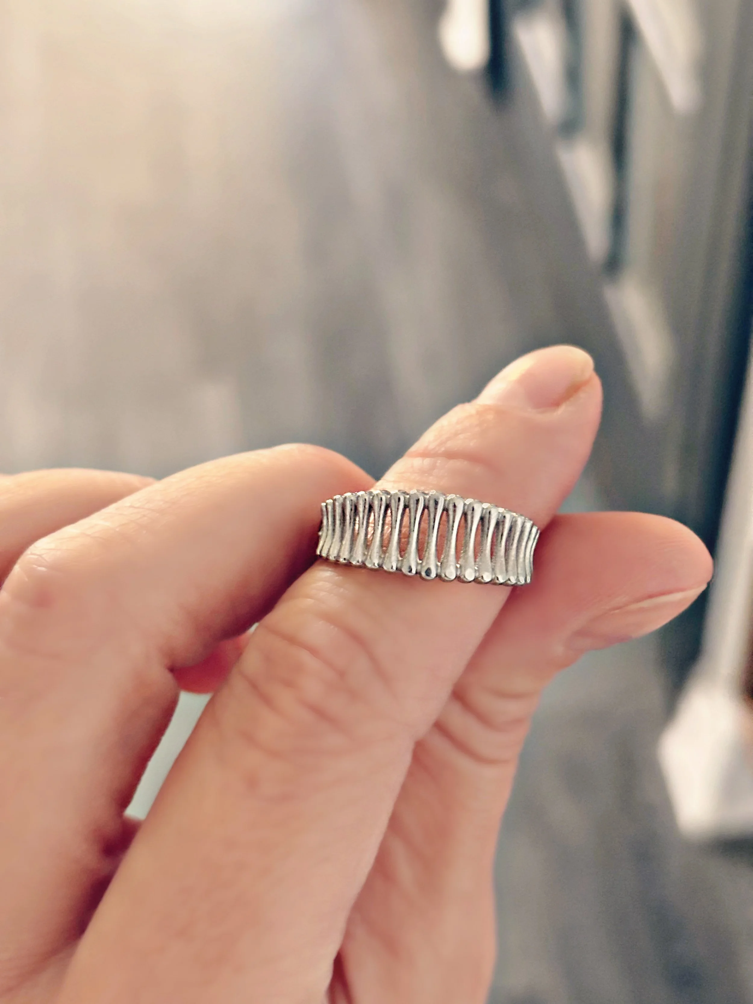 bague Ninon argentée tenue entre les doigts, design ajouré ajustable