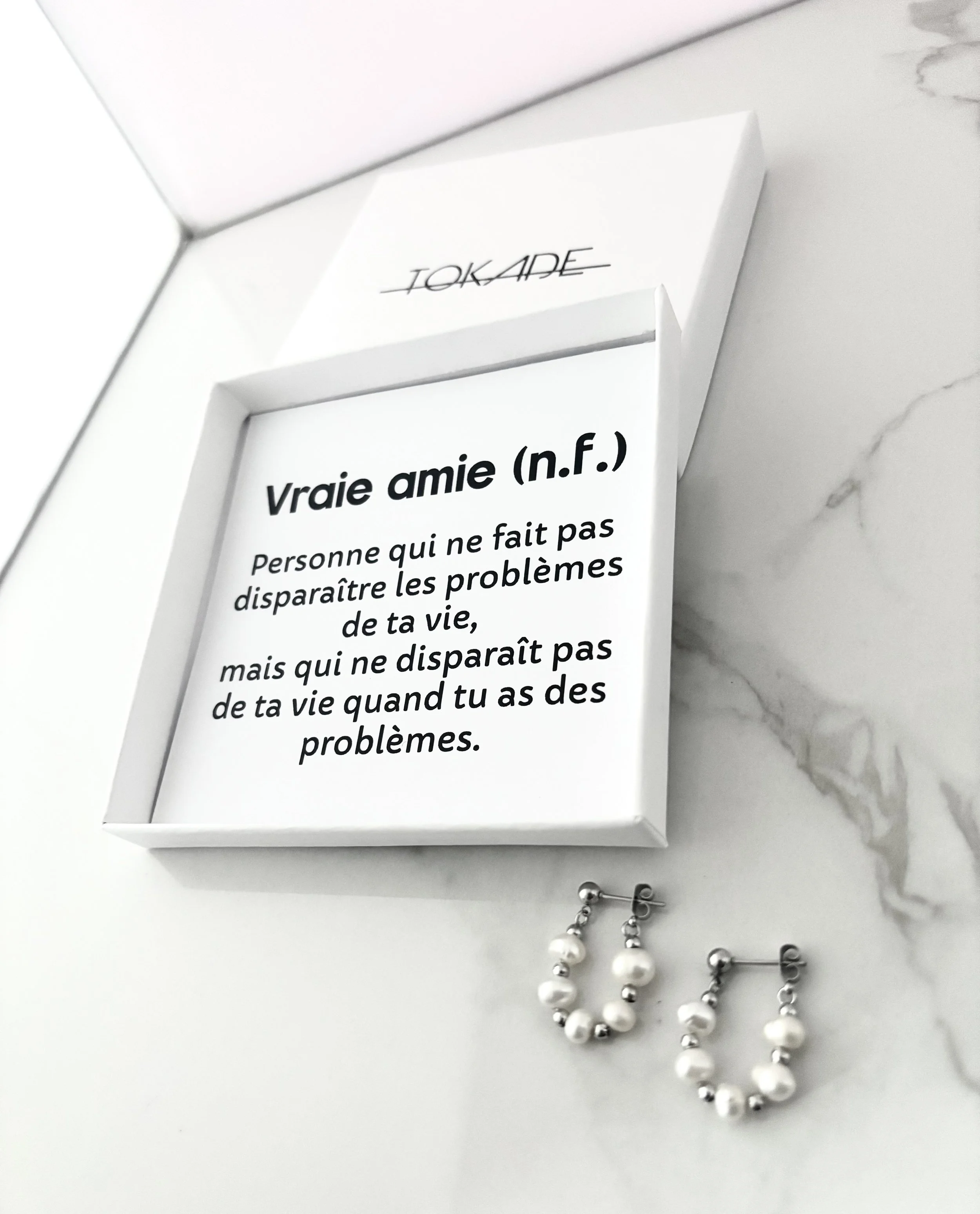 Coffret cadeau ouvert : message imprimé « Vraie amie (n.f.)… » avec les boucles de perles présentées dans la boîte.