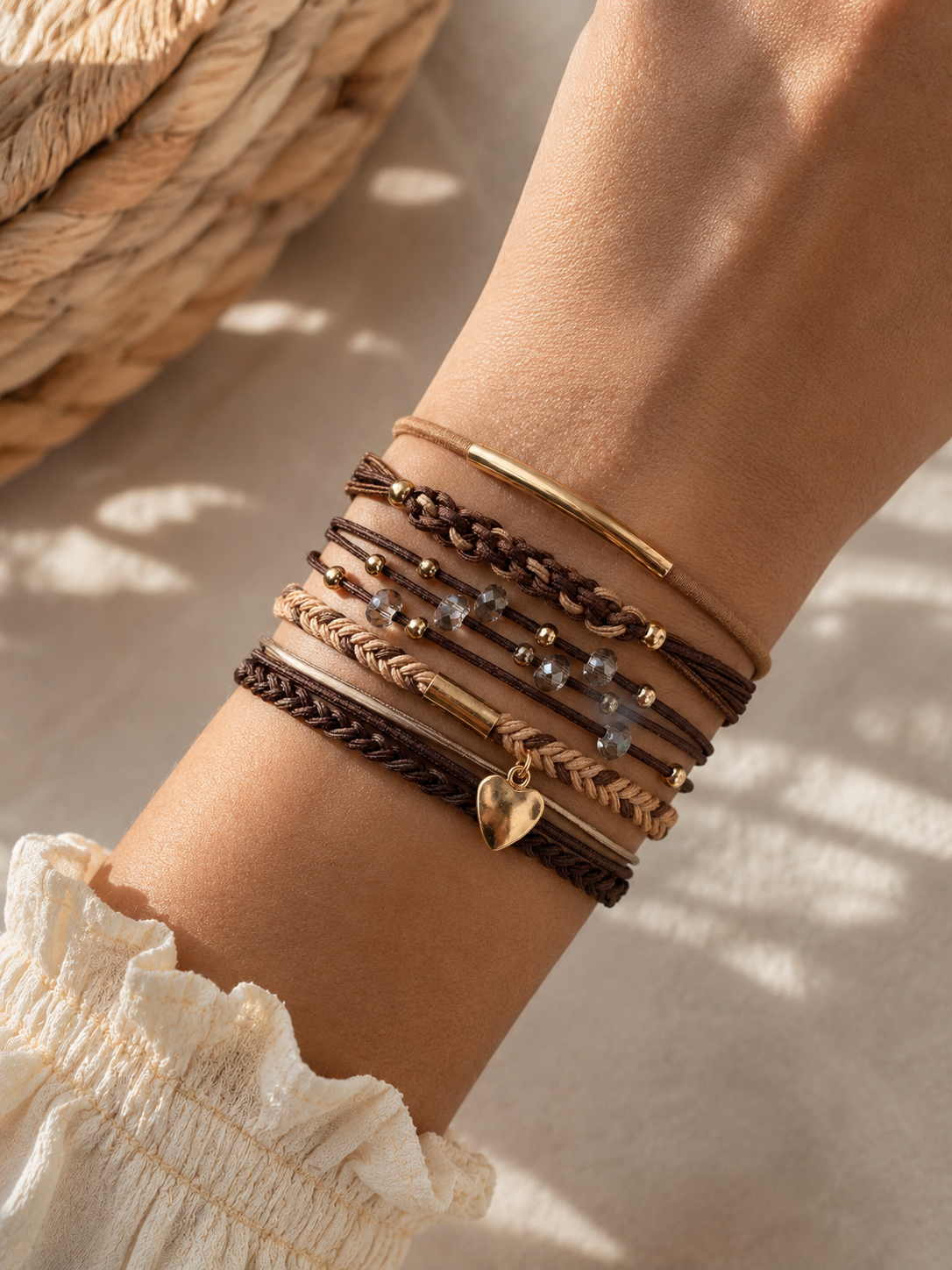 Lot de 5 élastiques à cheveux et bracelets 2-en-1 bohèmes en brun, beige et doré avec cristaux, tresses, perles et pendentif cœur, portés au poignet.