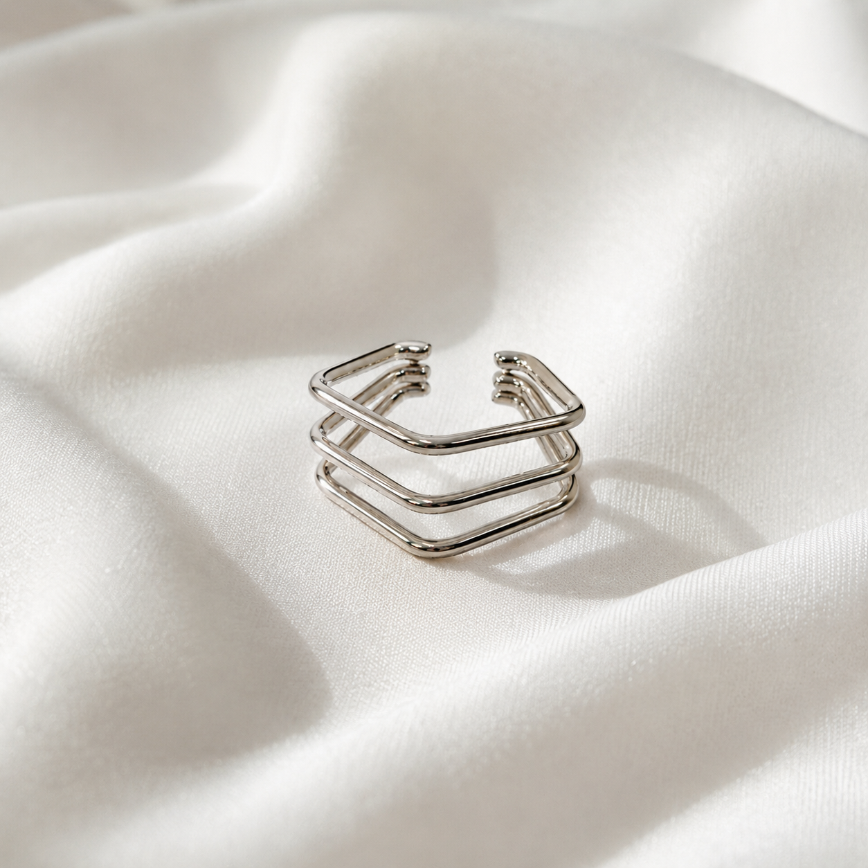 Anneau d’oreille Cassy argenté en acier inoxydable présenté sur un tissu blanc lumineux. - Tokade