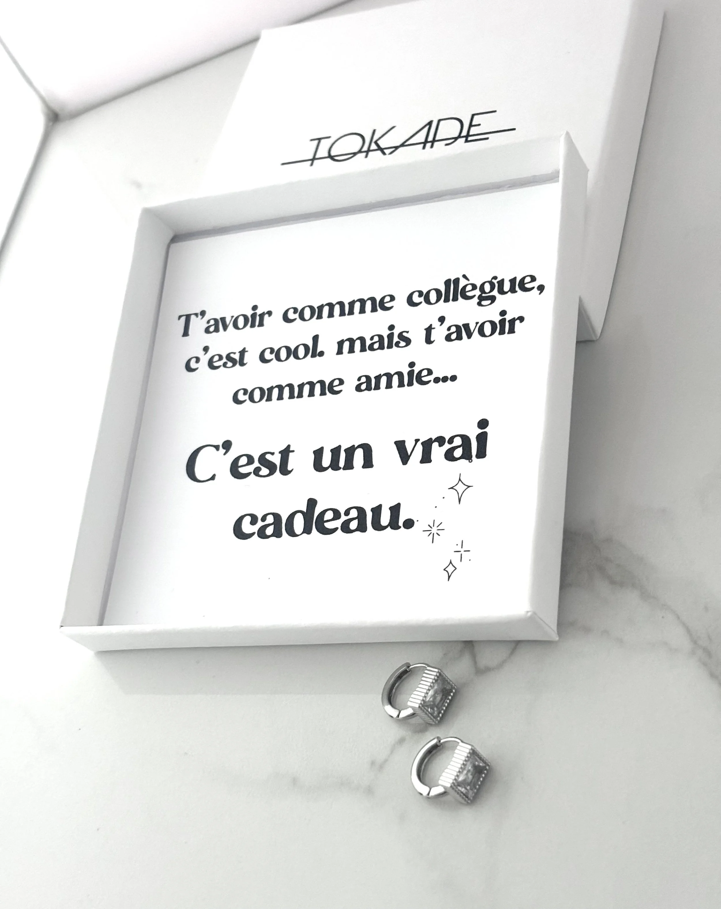 Coffret cadeau : message imprimé + boucles Laila en acier inoxydable argenté, présentation sur fond marbre.
