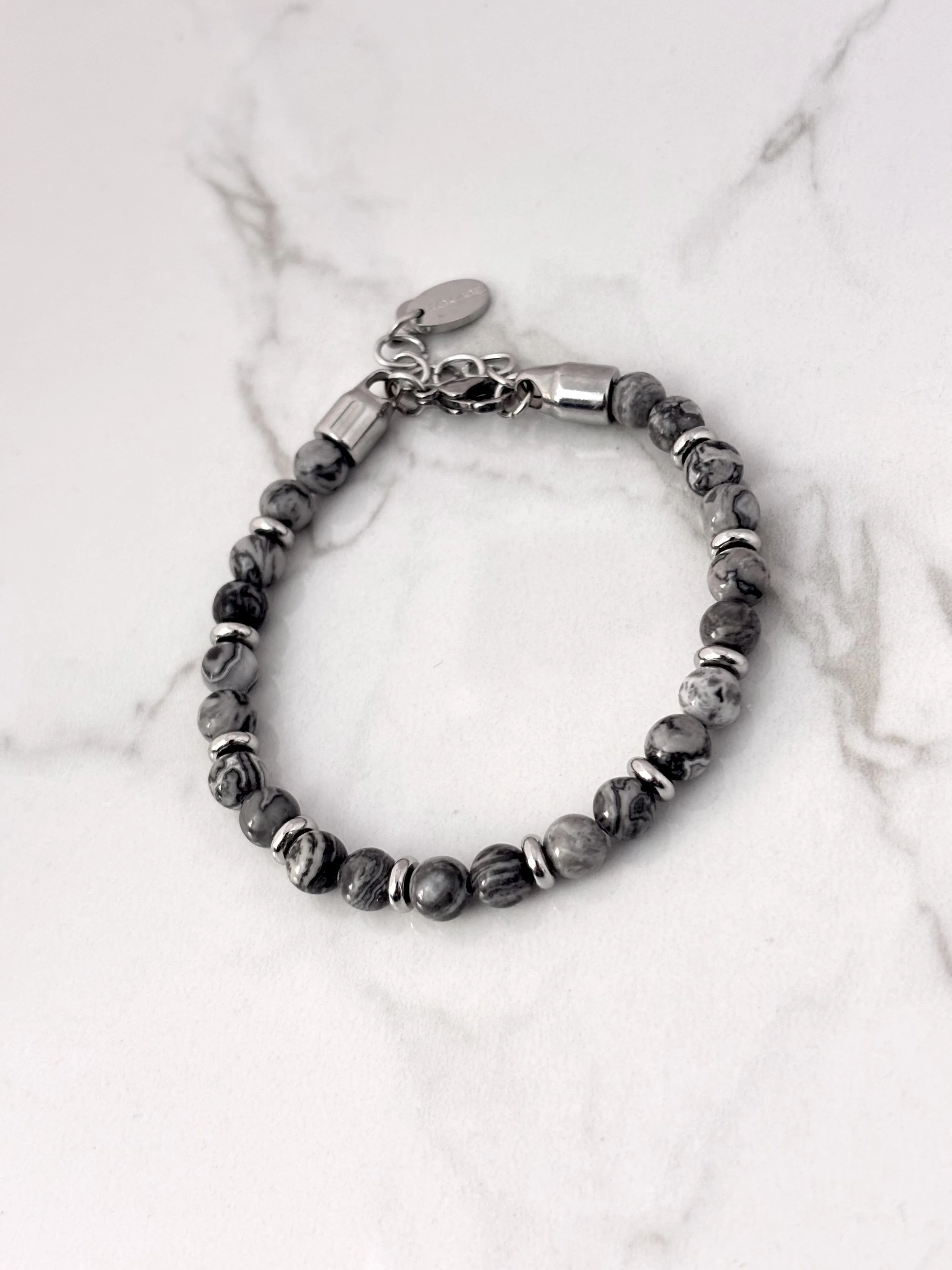 Bracelet en pierres naturelles grises et acier inoxydable sur fond marbré.