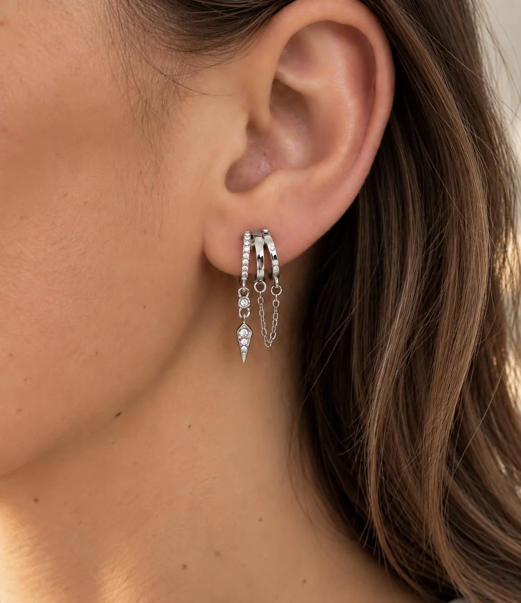 Boucles d’oreilles Jenna dorées à trois anneaux ornés de pierres brillantes et de chaînes pendantes, portées sur une oreille féminine.