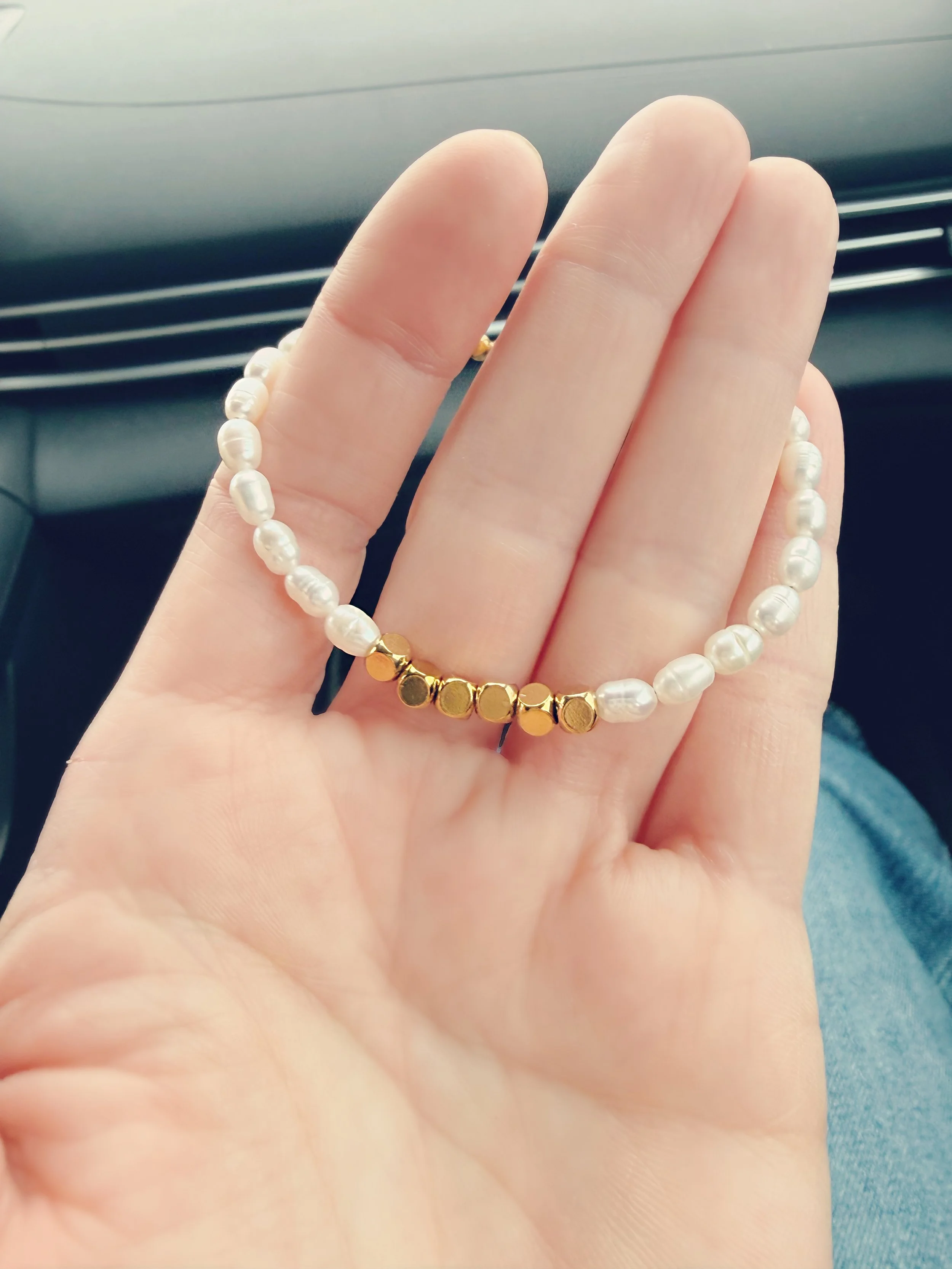 Bracelet perles blanches dans la main, détail du design en acier inoxydable