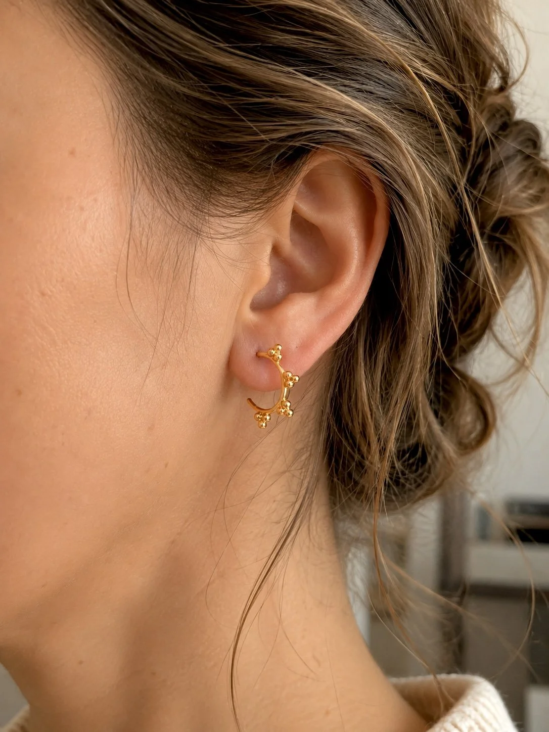 Femme portant les boucles d’oreilles Juli en acier inoxydable doré ornées de petites billes décoratives.