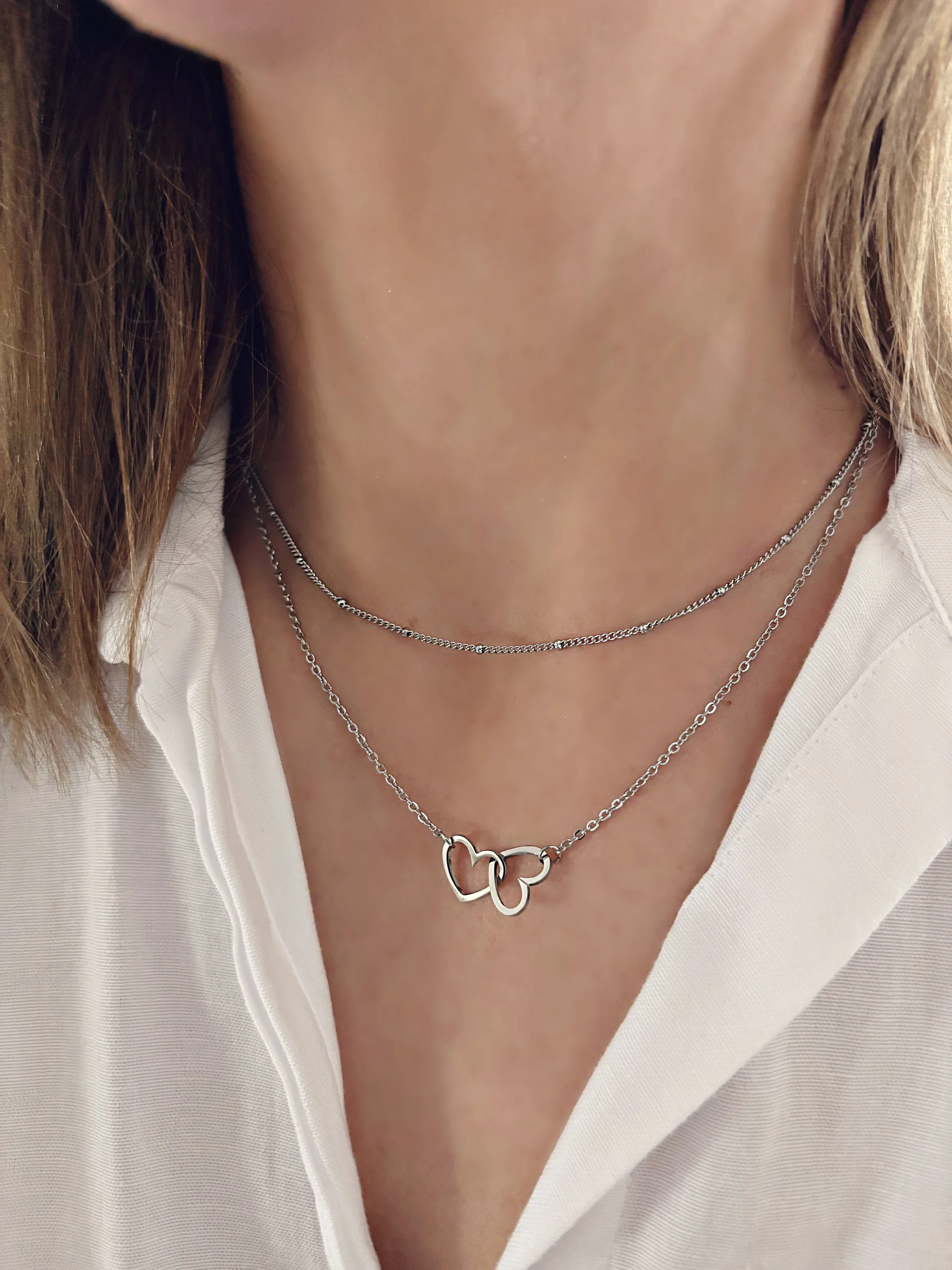 Collier Kalia porté, montrant les deux chaînes délicates et les pendentifs cœurs entrelacés sur un cou féminin.