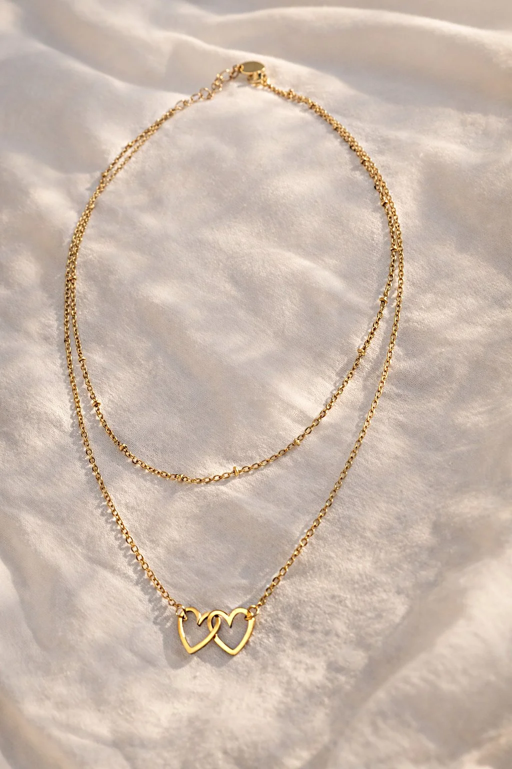 Collier cœurs doré présenté sur tissu clair lumineux-Tokade