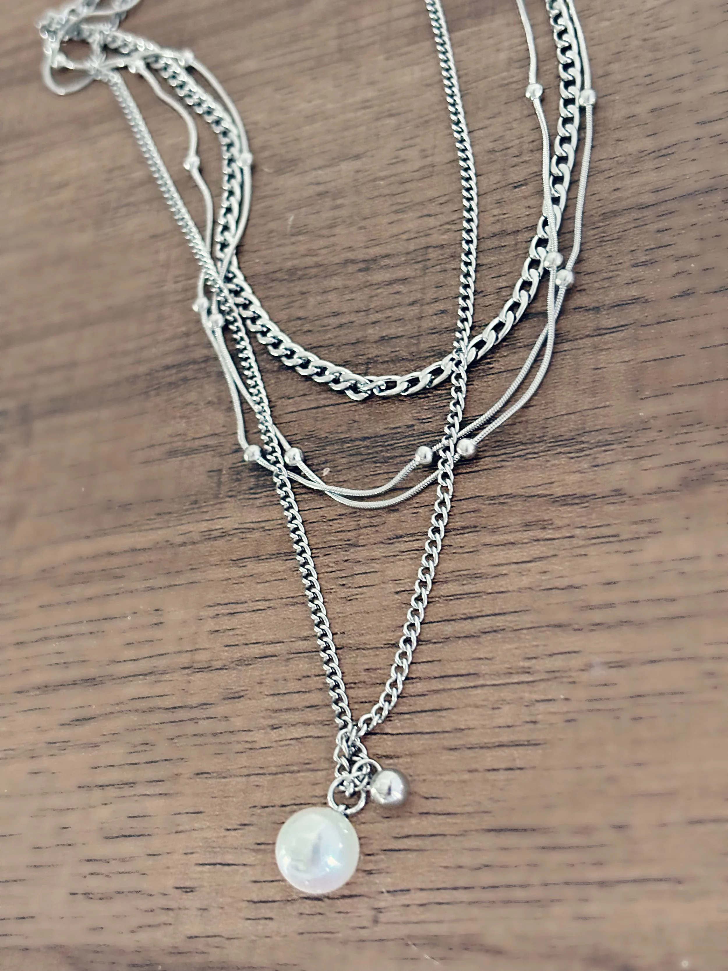Collier Maelis à plat sur une surface en bois, dévoilant les textures des chaînes et la brillance de la perle.