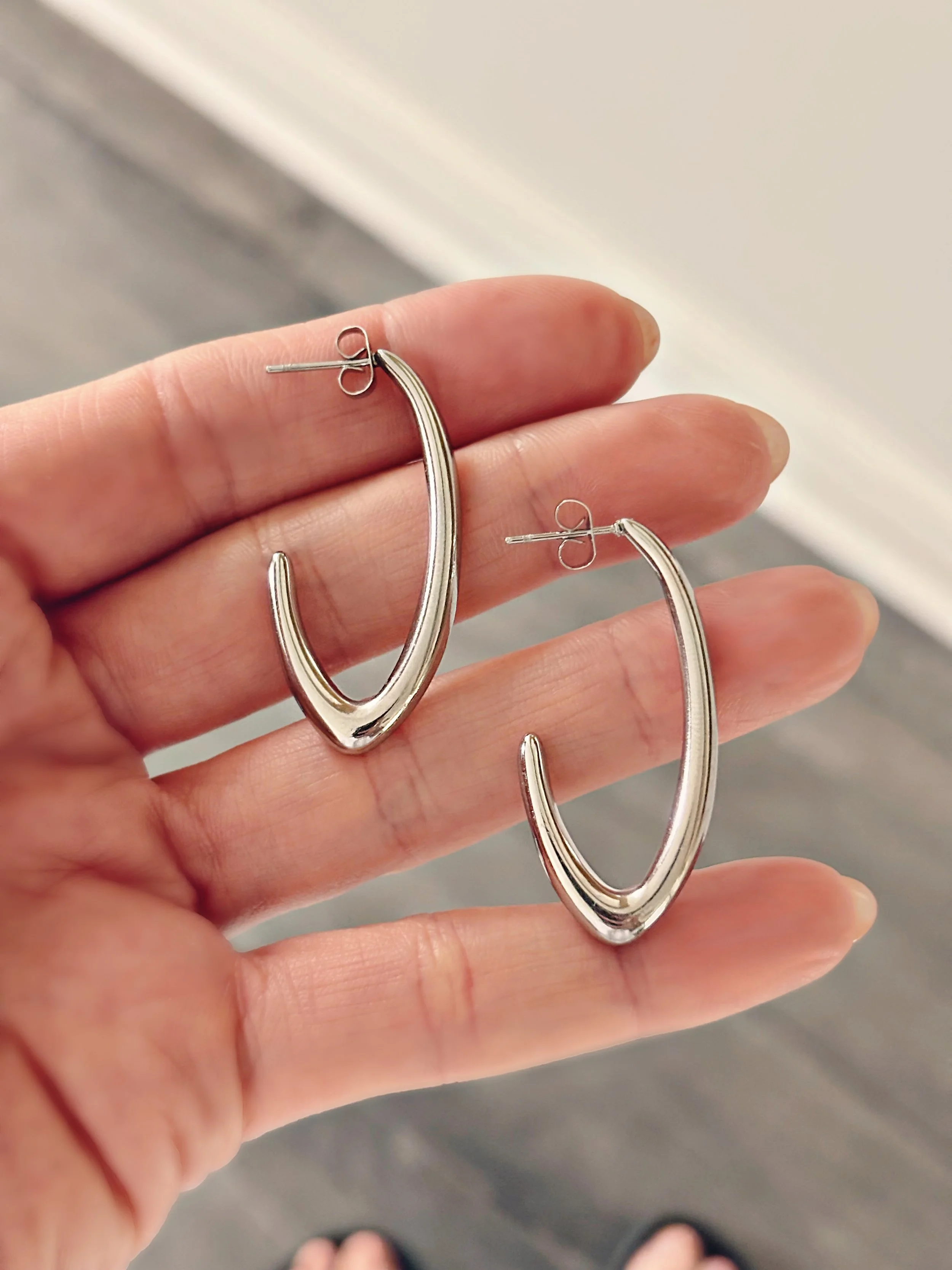 Boucles Amalia tenues dans la main, vue rapprochée sur leur forme audacieuse et lisse.