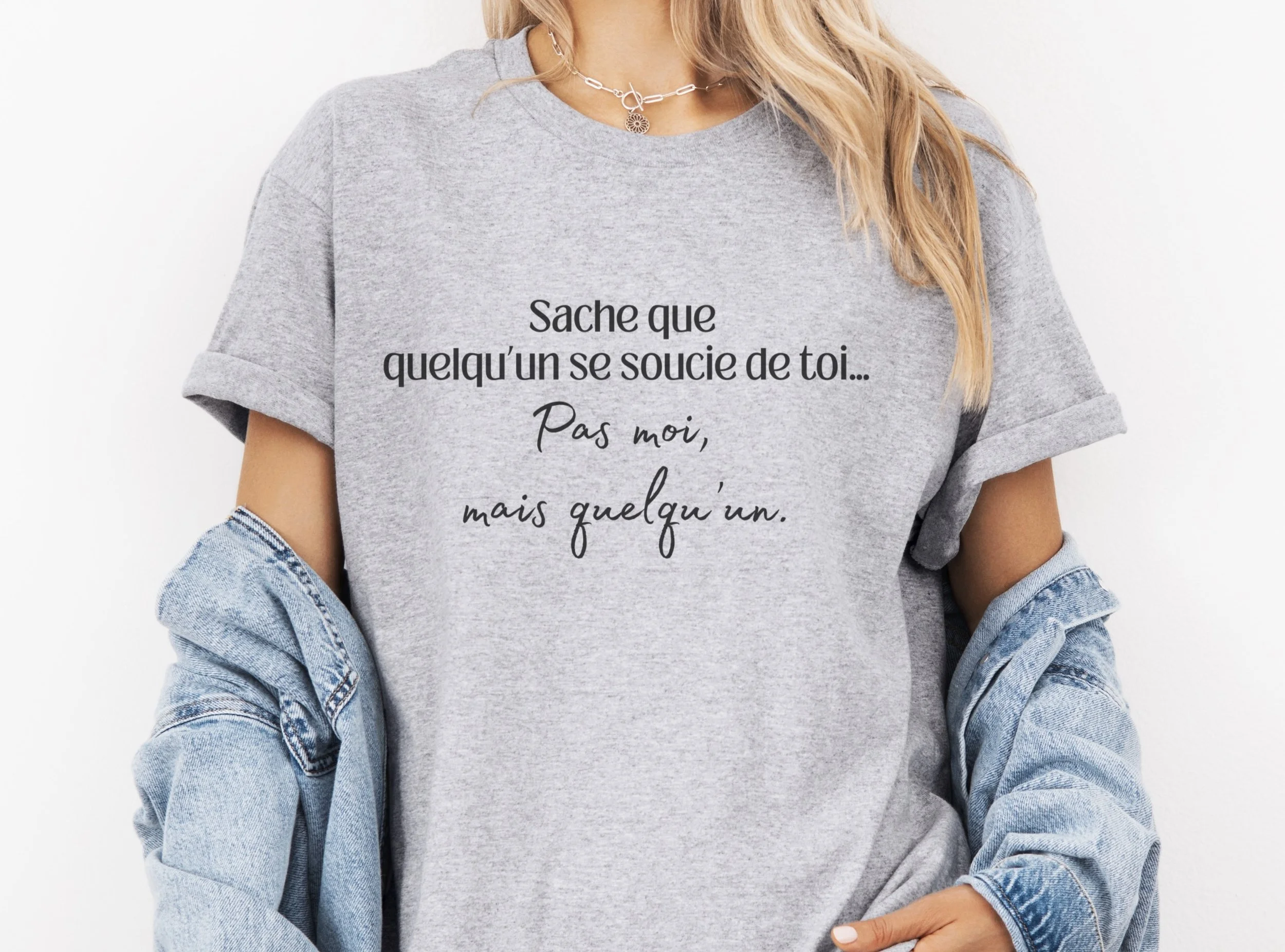 Femme portant un t-shirt gris avec l’inscription « Sache que quelqu’un se soucie de toi… Pas moi, mais quelqu’un. » — Tokade