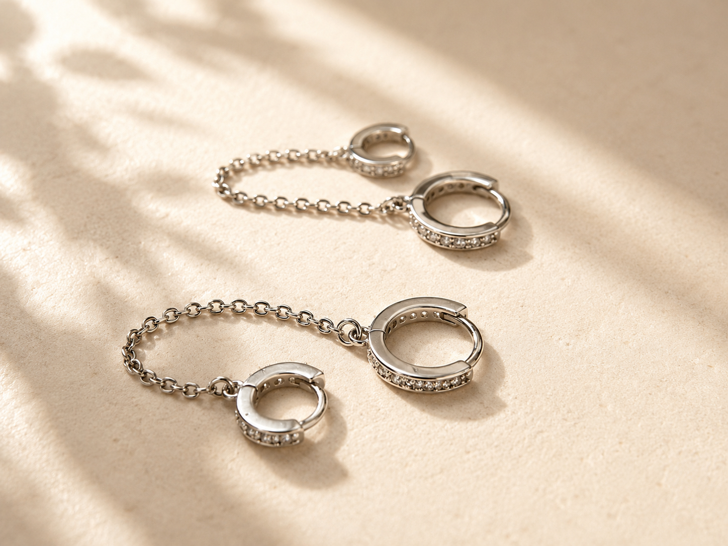 Boucles d’oreilles Tessy en acier inoxydable avec chaîne et cristaux sur fond crème lumineux - Tokade