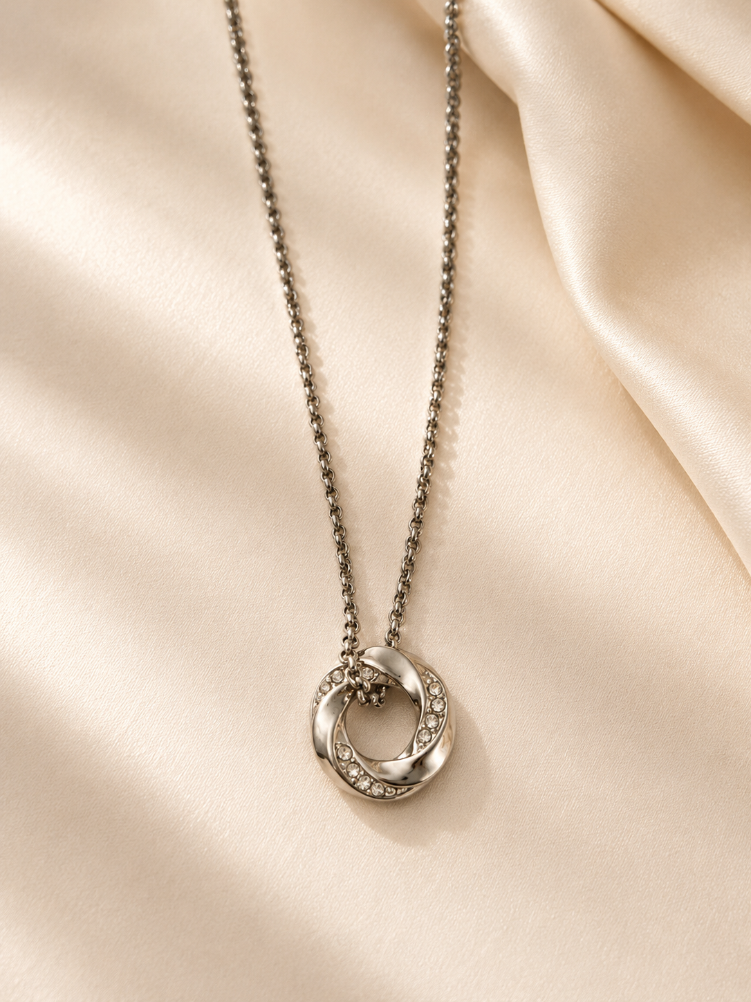 Collier Oma en acier inoxydable avec cristaux présenté sur un tissu satiné beige lumineux. - Tokade