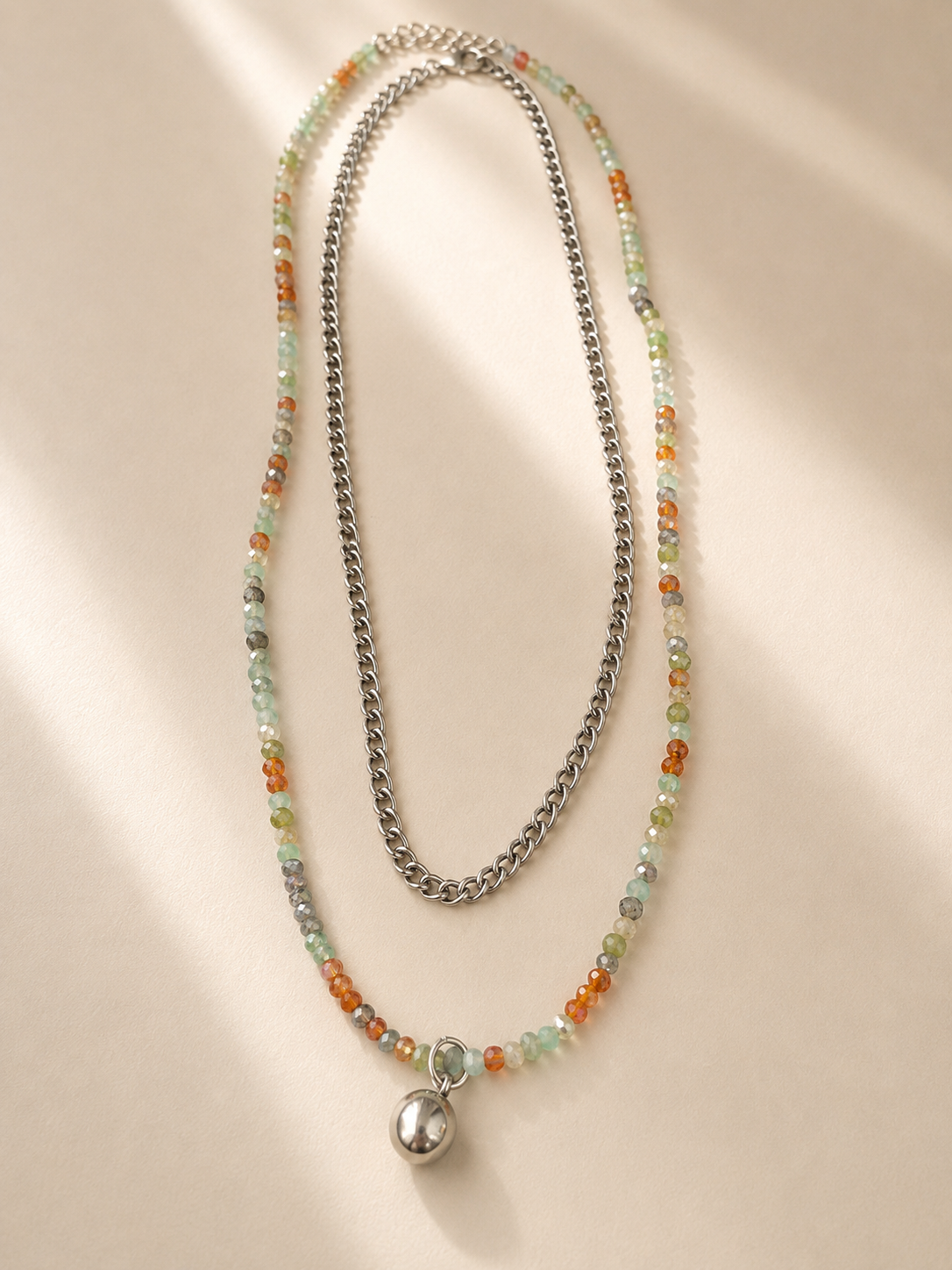 Collier Maya double rang en acier inoxydable argenté avec pierres naturelles multicolores et pendentif sphérique sur fond crème. -Tokade