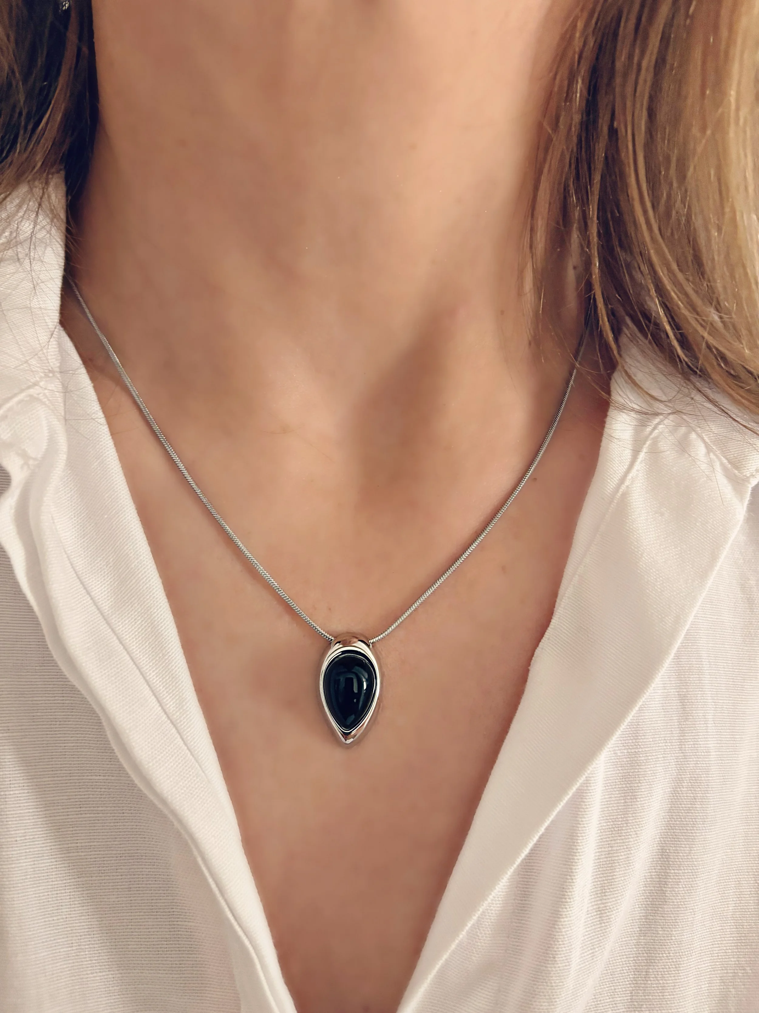 Le collier Selina porté, mettant en valeur la pierre noire et le pendentif goutte contre une chemise blanche.