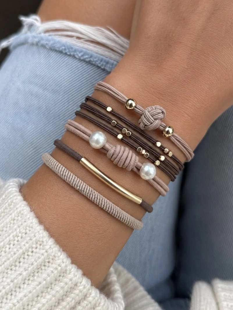 Lot de 5 élastiques à cheveux et bracelets 2-en-1 beige, brun et taupe avec perles, nœuds décoratifs et détails dorés.