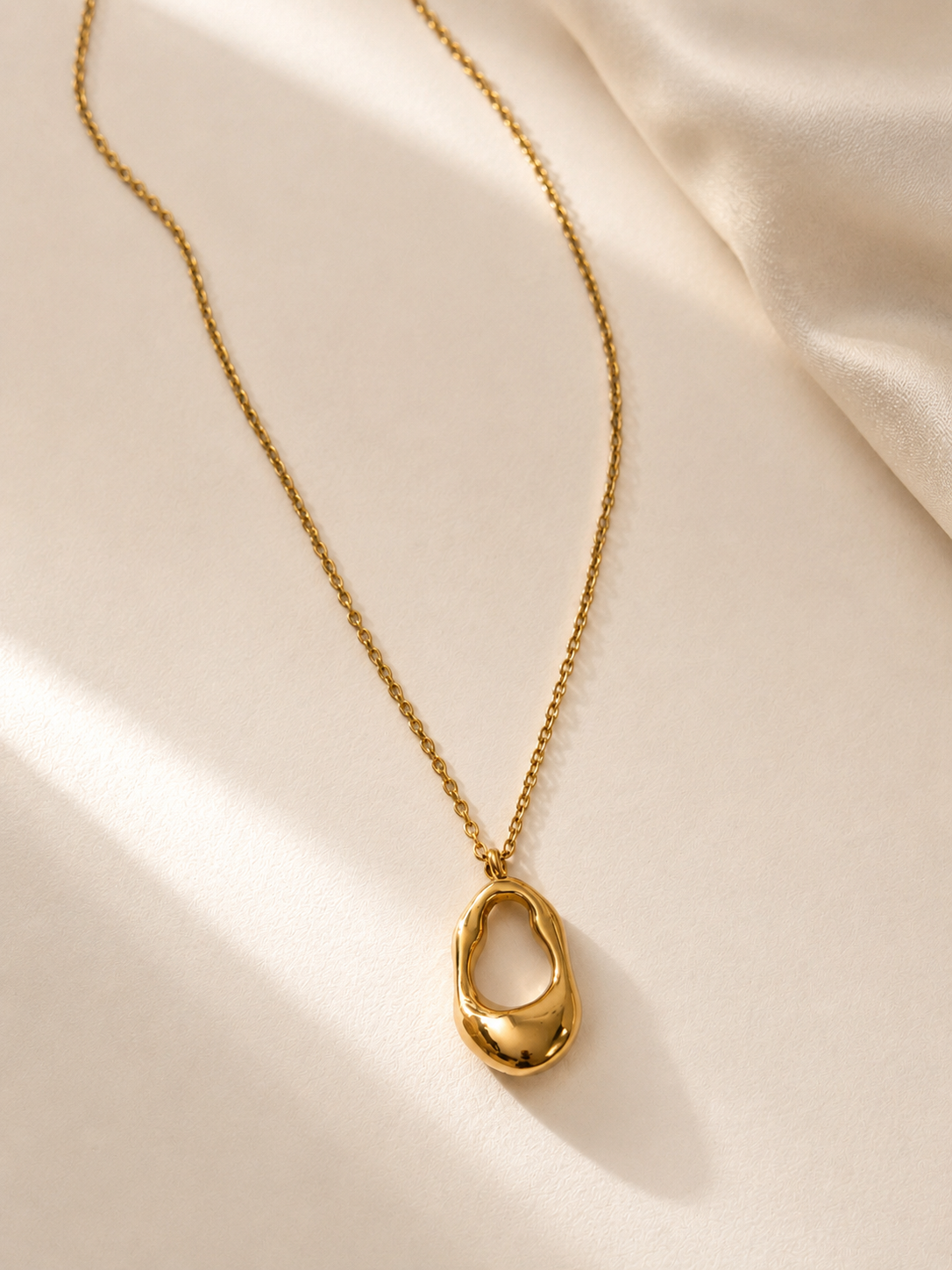 Collier Galos en acier inoxydable doré présenté sur un tissu satiné crème. - Tokade