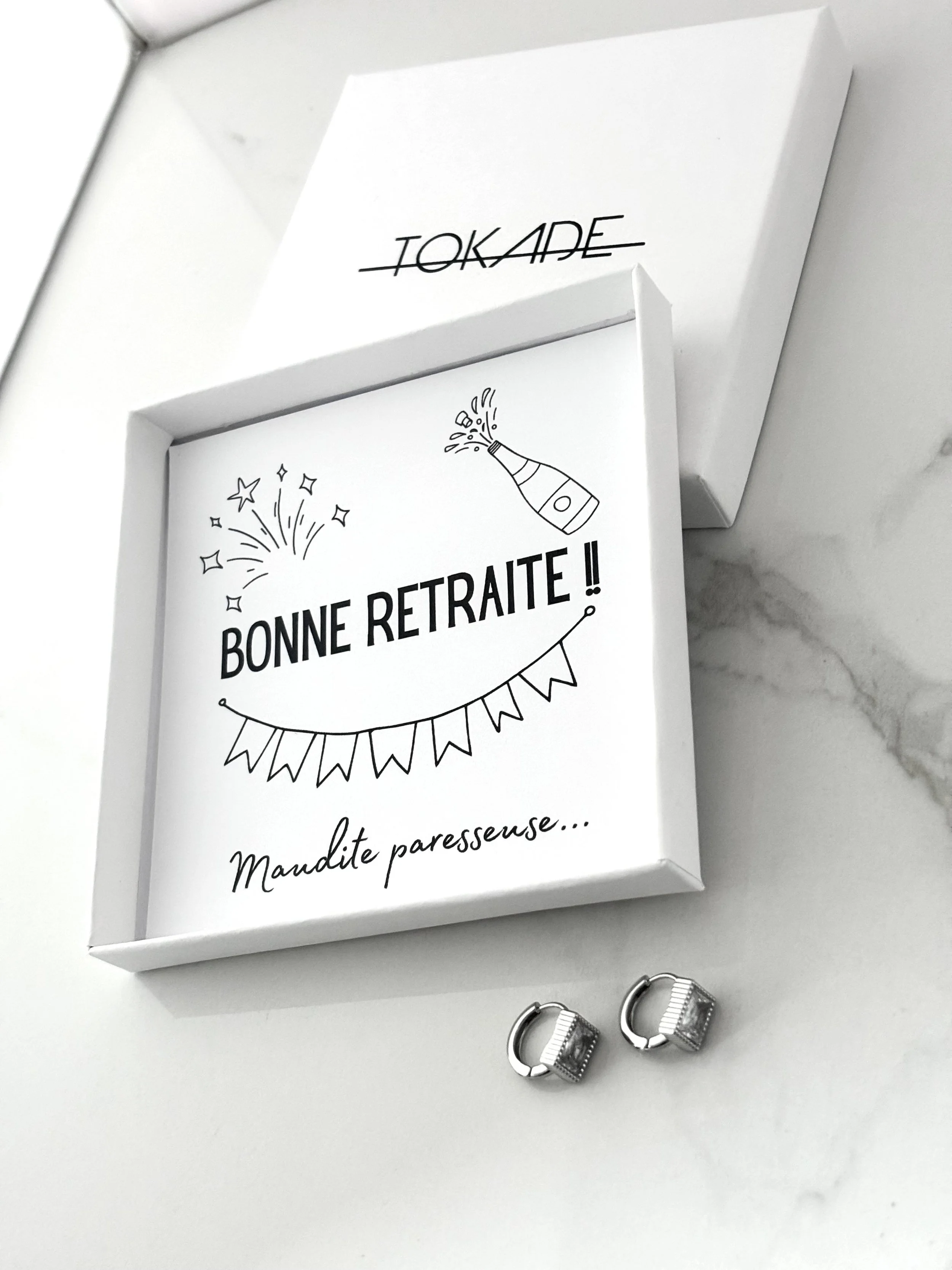 Boîte cadeau humoristique Bonne retraite !! Maudite paresseuse… avec boucles d’oreilles Laila en acier inoxydable Tokade, présentée dans un écrin blanc chic.