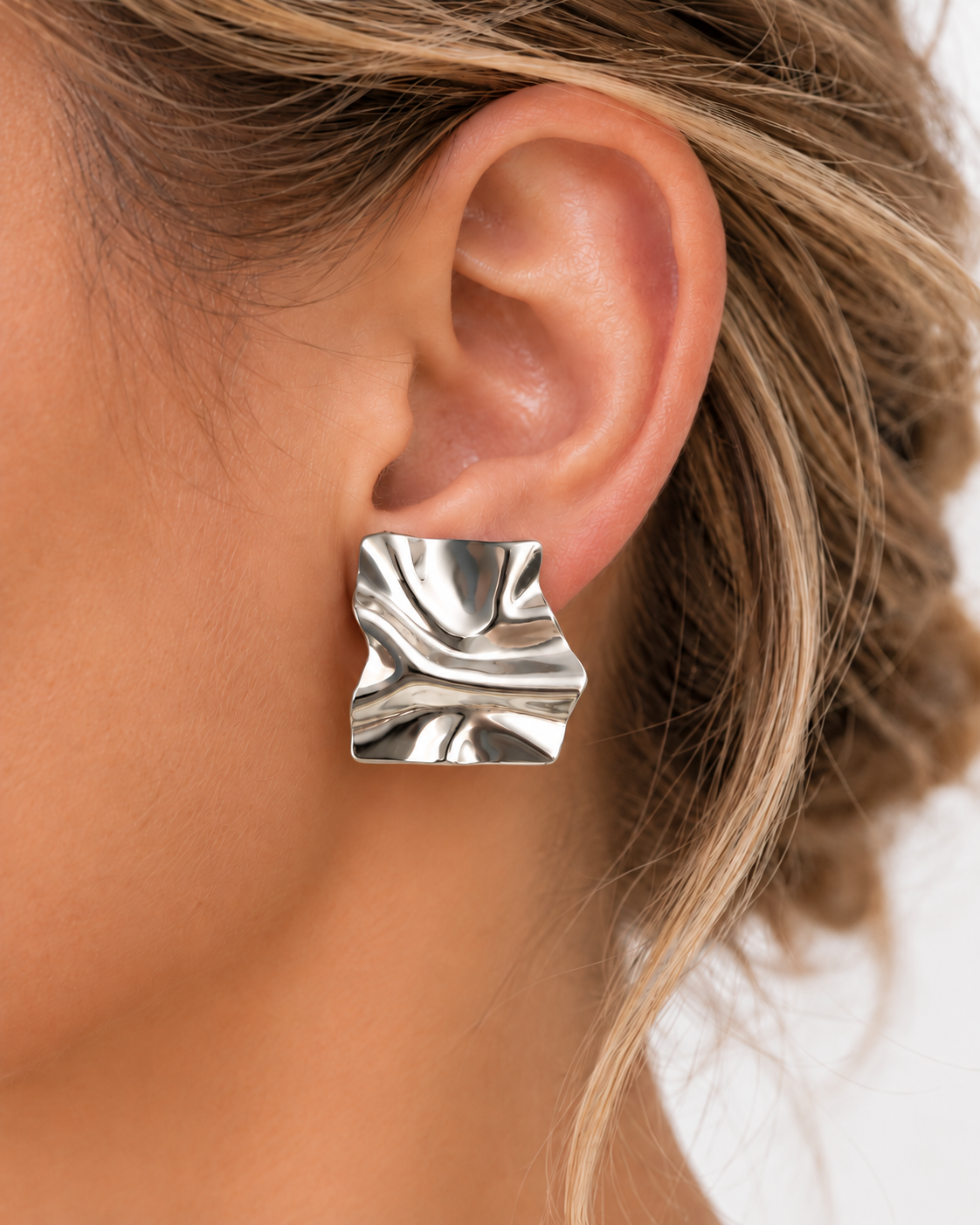 Boucle d’oreille Annita argentée portée sur une oreille féminine, forme carrée ondulée et fini miroir brillant en acier inoxydable.