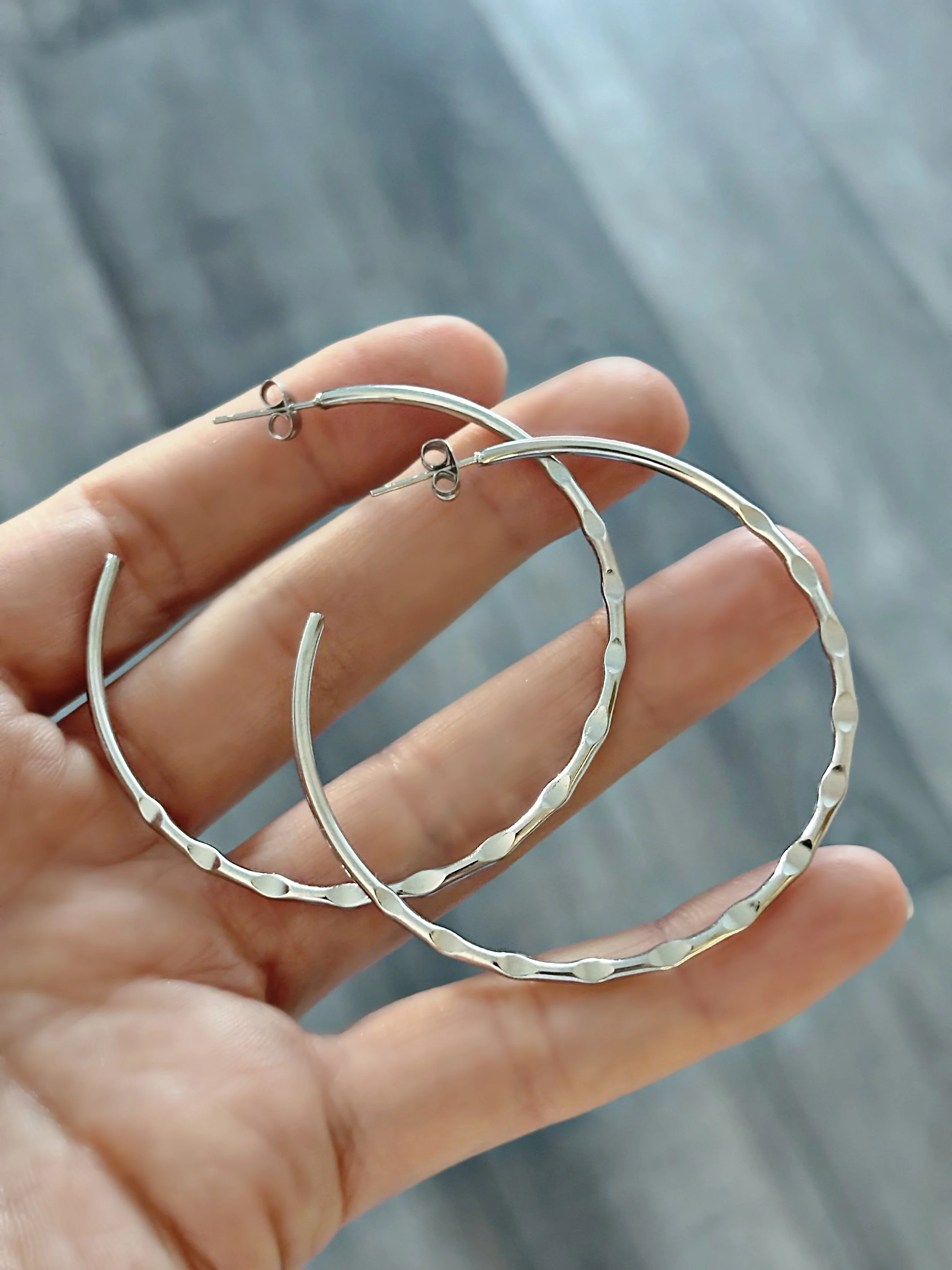 Boucles d’oreilles Sienna en acier inoxydable argentées, grands anneaux ondulés posés dans une main – Tokade