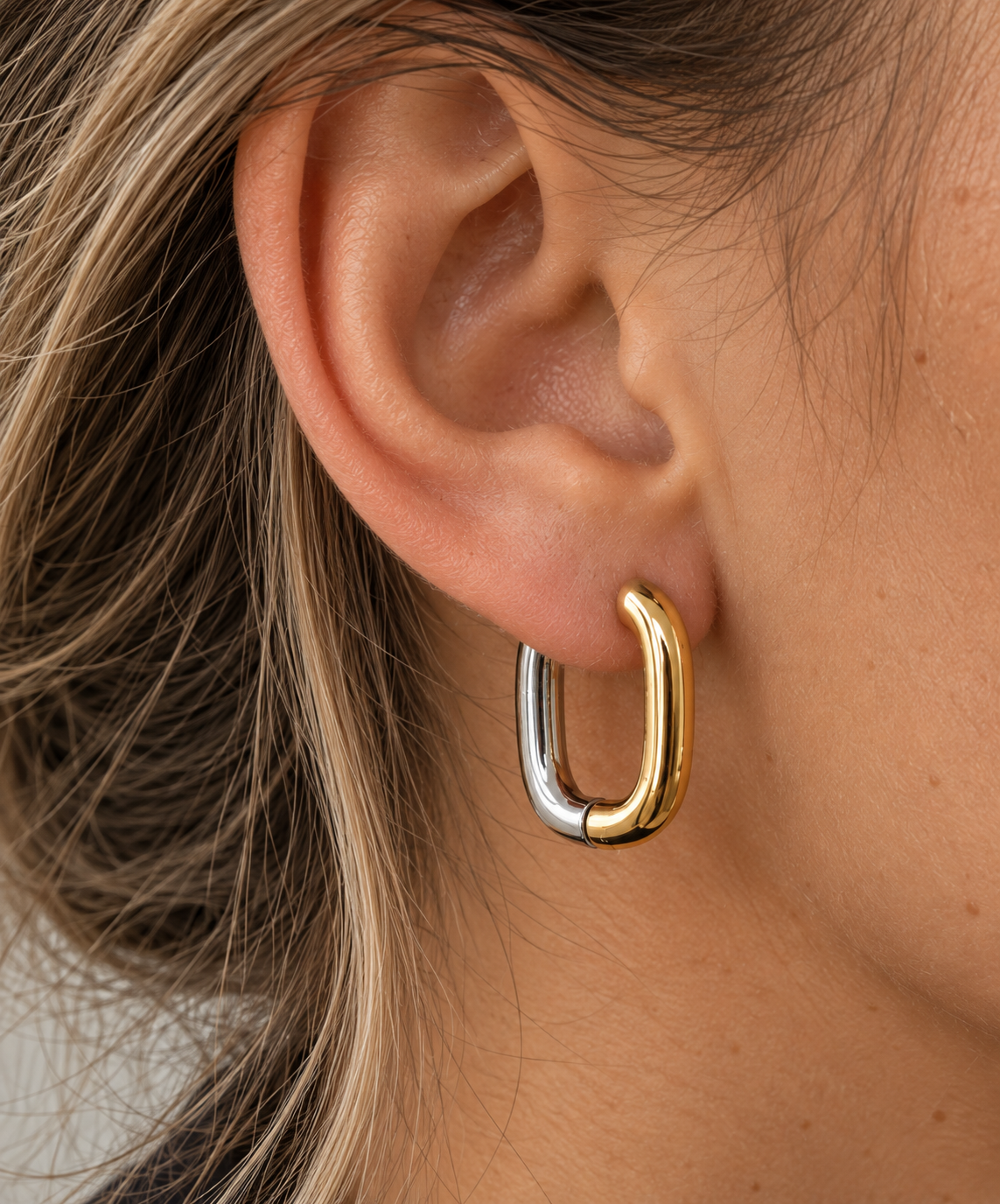 Boucle d’oreille Éos bicolore personnalisable portée sur une oreille féminine, anneau rectangulaire doré et argenté.