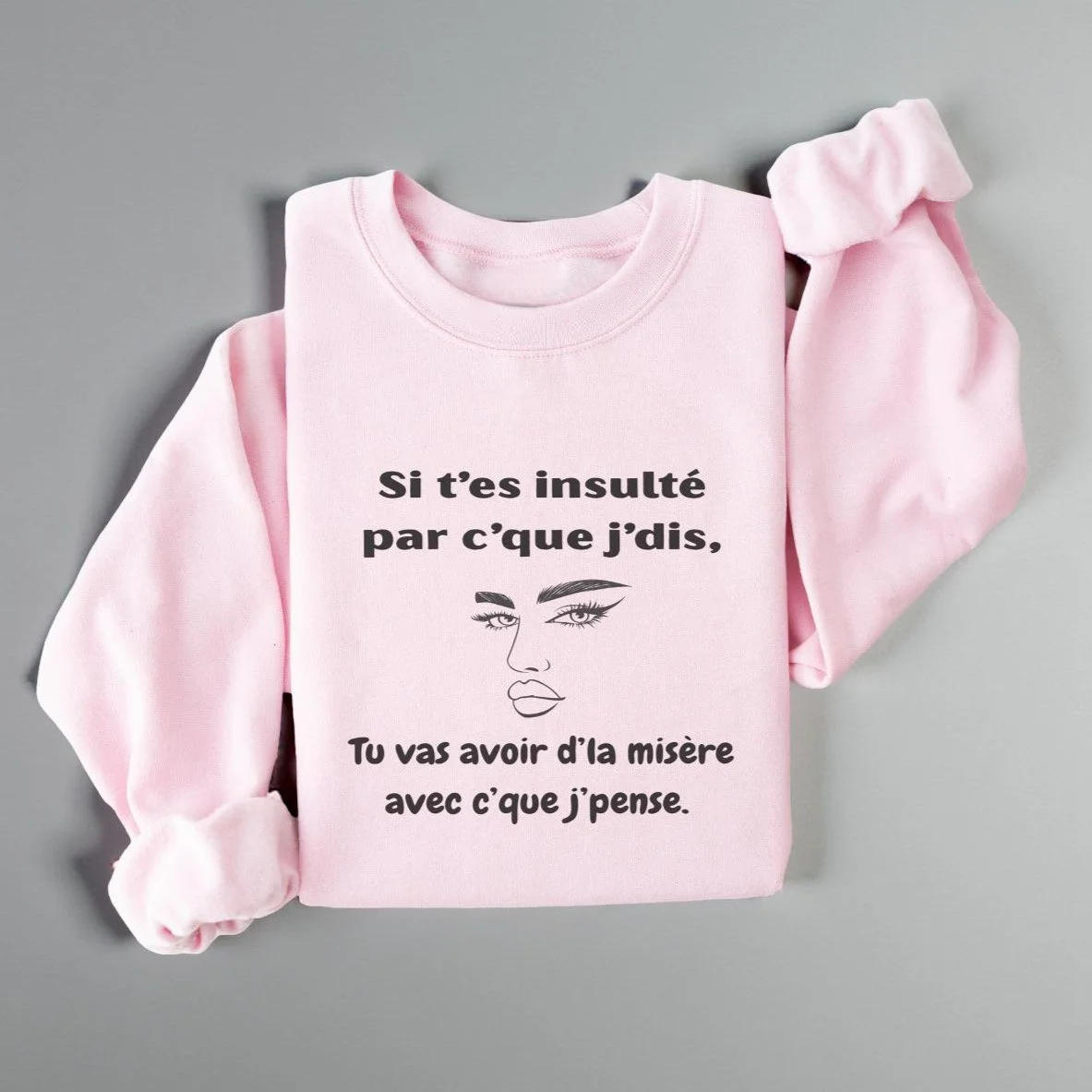 Coton ouaté gris avec le texte « Si t’es insulté par c’que j’dis » plié sur une table en bois