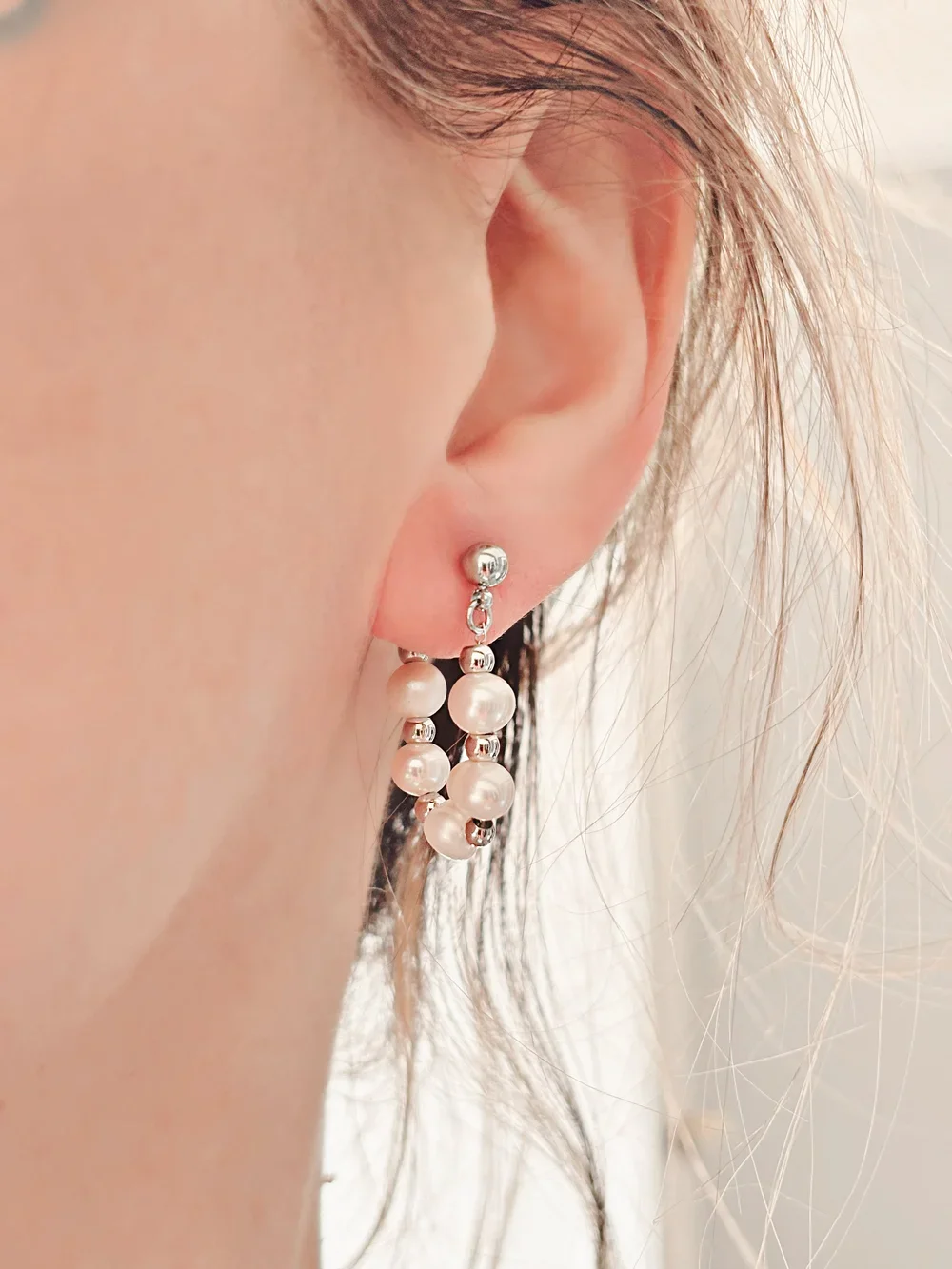 Gros plan des boucles portées ou déposées sur fond clair montrant les détails des perles et billes argentées.