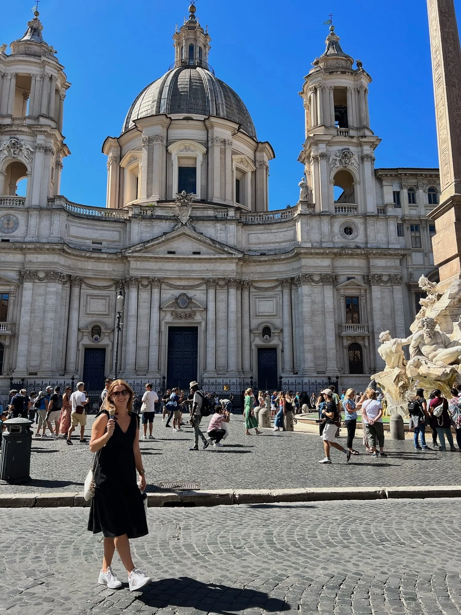 woman in front of rome building and fountain while eating gelato in black dress