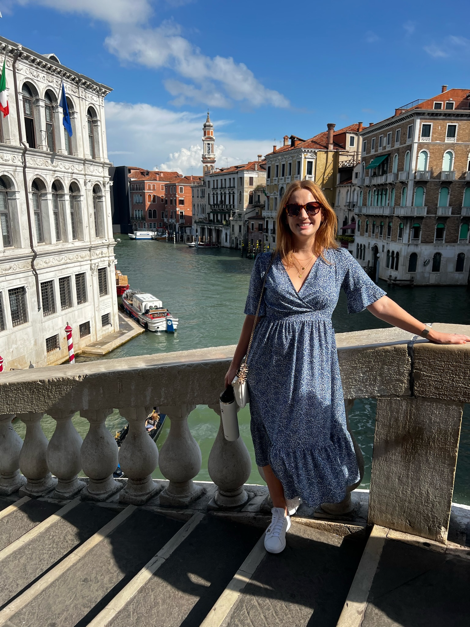 red haired woman in blue dress posing on bridge in venezia with canals and buildings in background