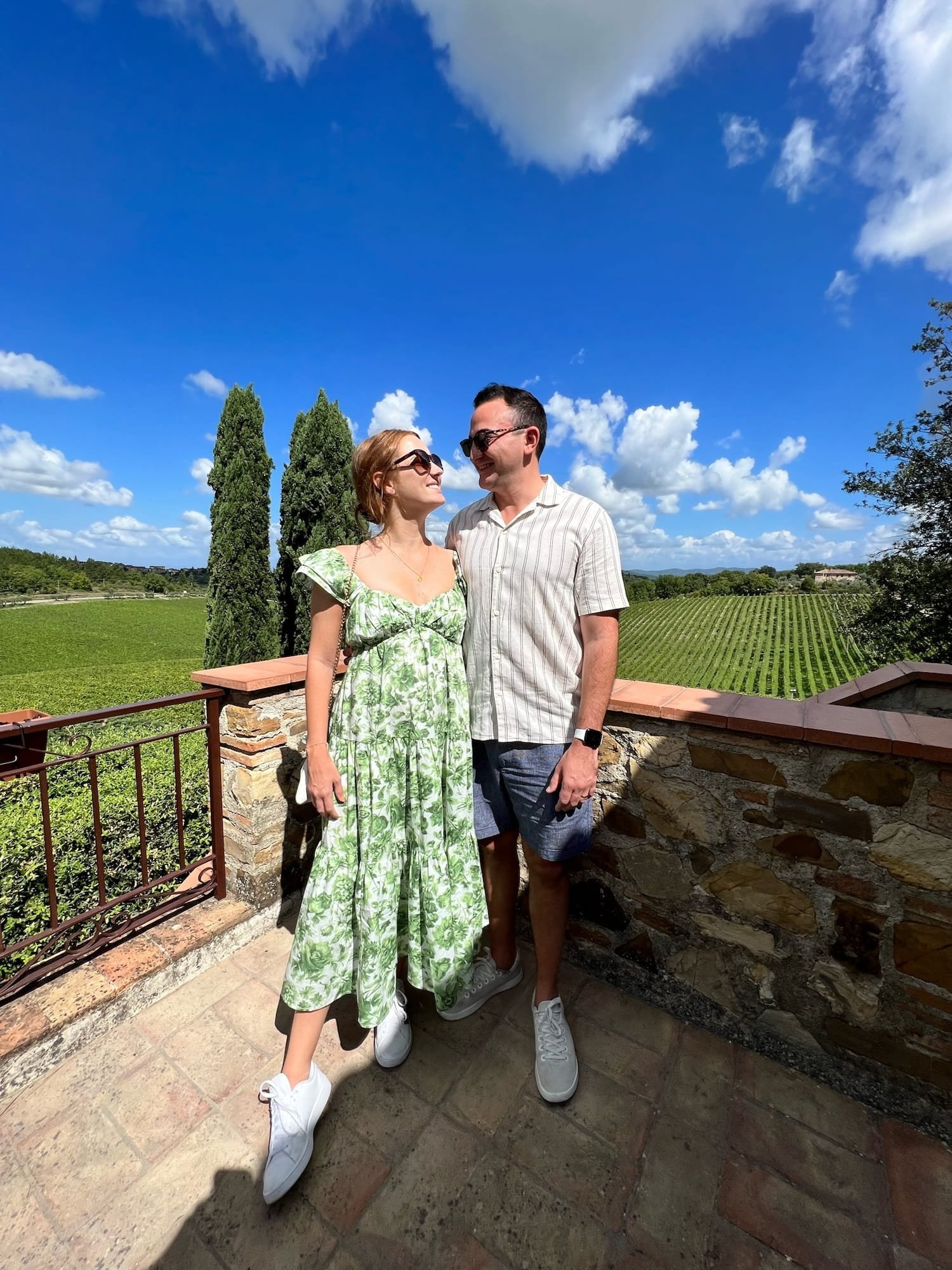 woman in green floral dress looking at man while wine tasting in beautiful tuscany at Casa Emma with vineyard in the background