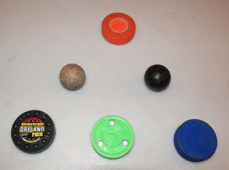 Various stickhandling objects are available. The Dryland Puck (bottom left) costs $12 and is purported to be viable on a sliding surface or floor. In my opinion, it performs poorly in both settings. The Green Biscuit, which sells for about $13, slides okay on a slippery surface but feels heavier and clunkier than a puck on ice. The blue puck ($2) is like a regular puck except it's two ounces lighter. It works fairly well on a shooting pad. The Swedish Ball ($4, second row, left) is a very lightweight wooden ball that really flies around a shooting pad. It's good for working on quick hands. The Extreme Stickhandling Ball ($9, second row, right) is heavy and hard. Surprisingly, on a shooting pad it has a feel similar to a puck on ice. The basic orange floor hockey puck ($2), slides nicely on a floor or shooting pad.