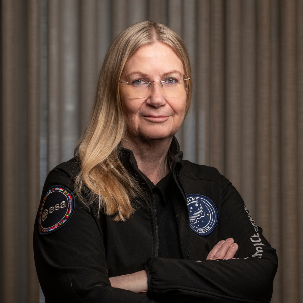 Woman in black NASA and ESA jacket with arms crossed, standing in front of a curtain.
