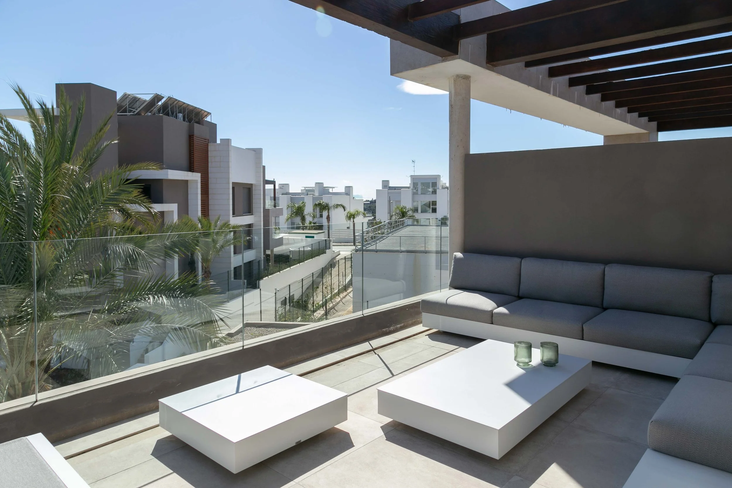 Balcony view with modern white buildings, green palm trees, and clear blue sky