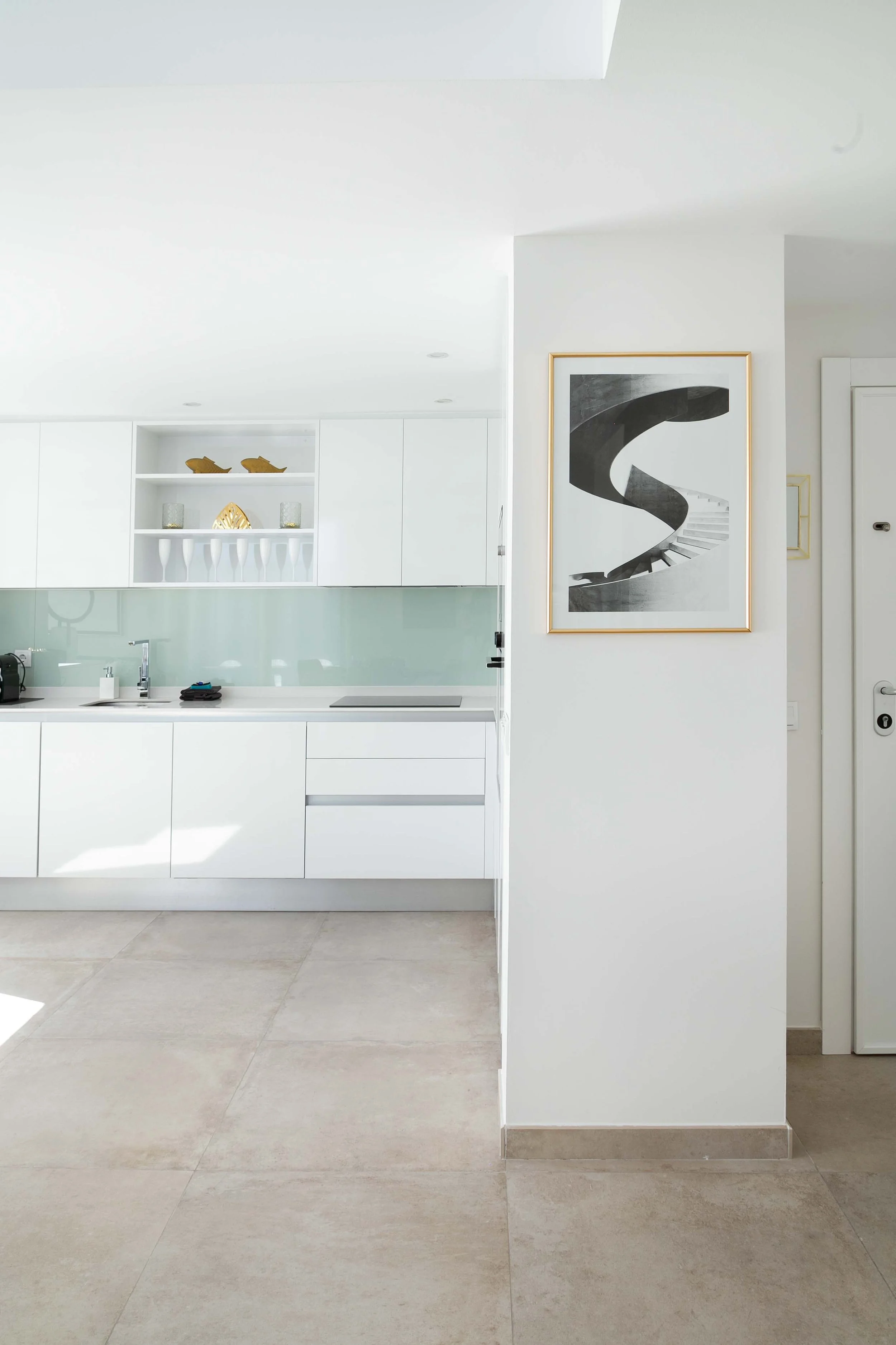 Modern kitchen with white cabinetry, a light green backsplash, and a large black and white spiral staircase artwork on the wall.