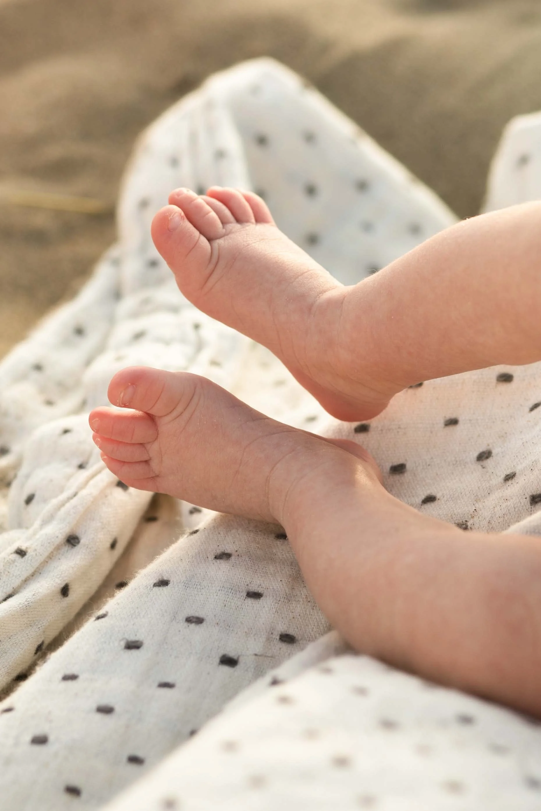 Close-up of a baby’s hand resting on an adult’s hand, with the adult wearing white pajamas with black polka dots, sitting on a surface with a blurred background.