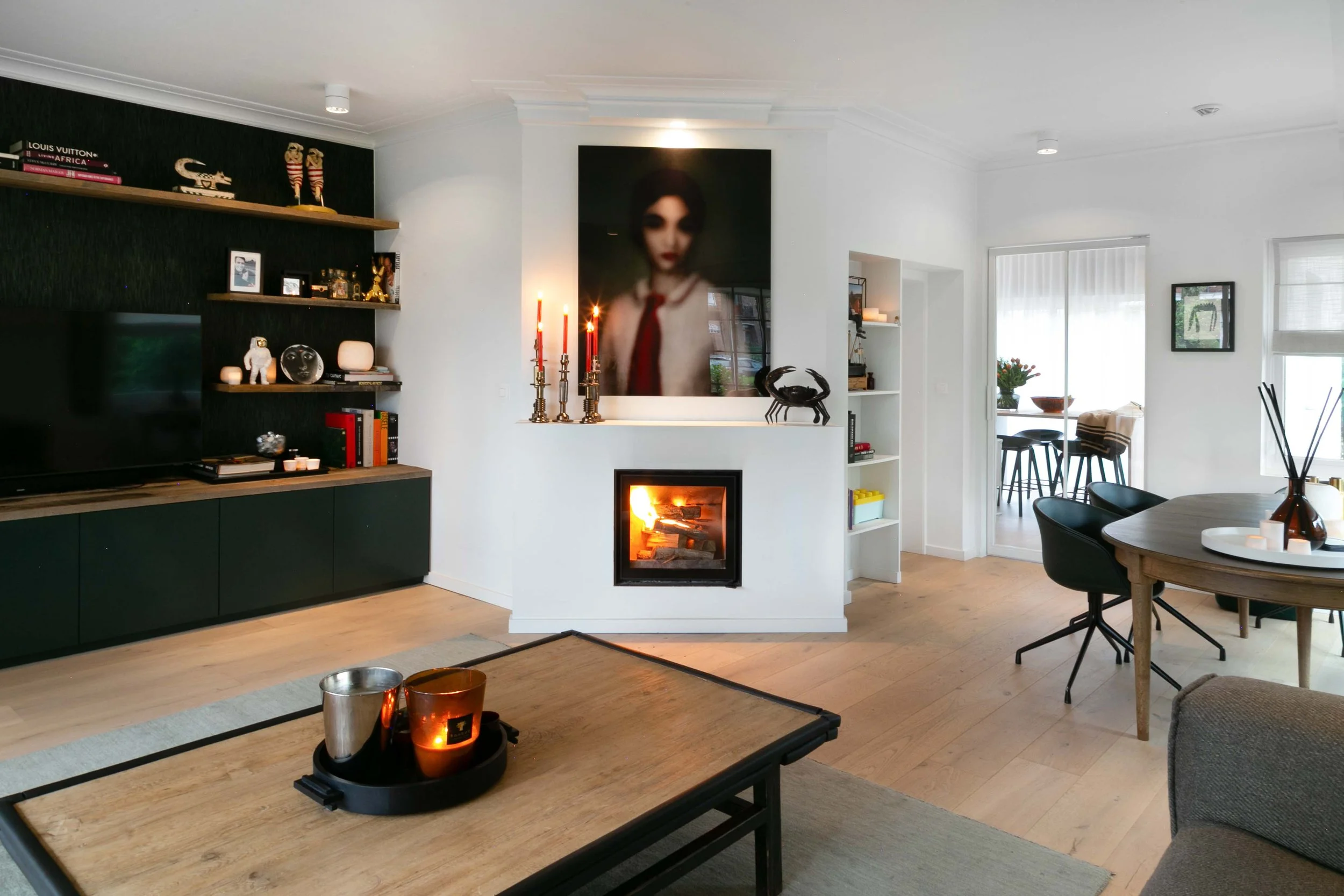 Living room with a fireplace, black and white furniture, decorative shelves, and large wall art of a person's face.