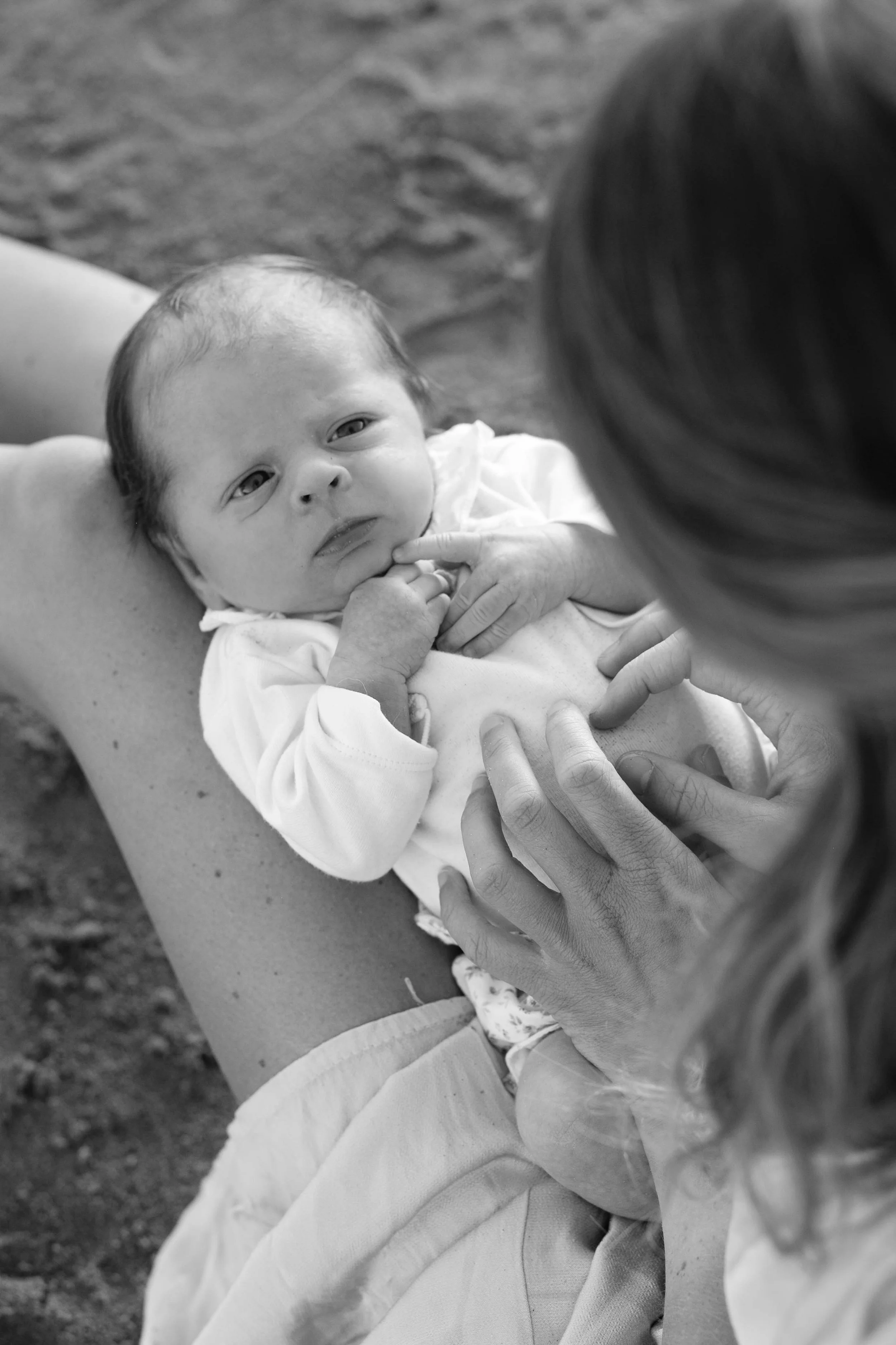 A newborn baby looking at a woman whose face is not visible in black and white photography.